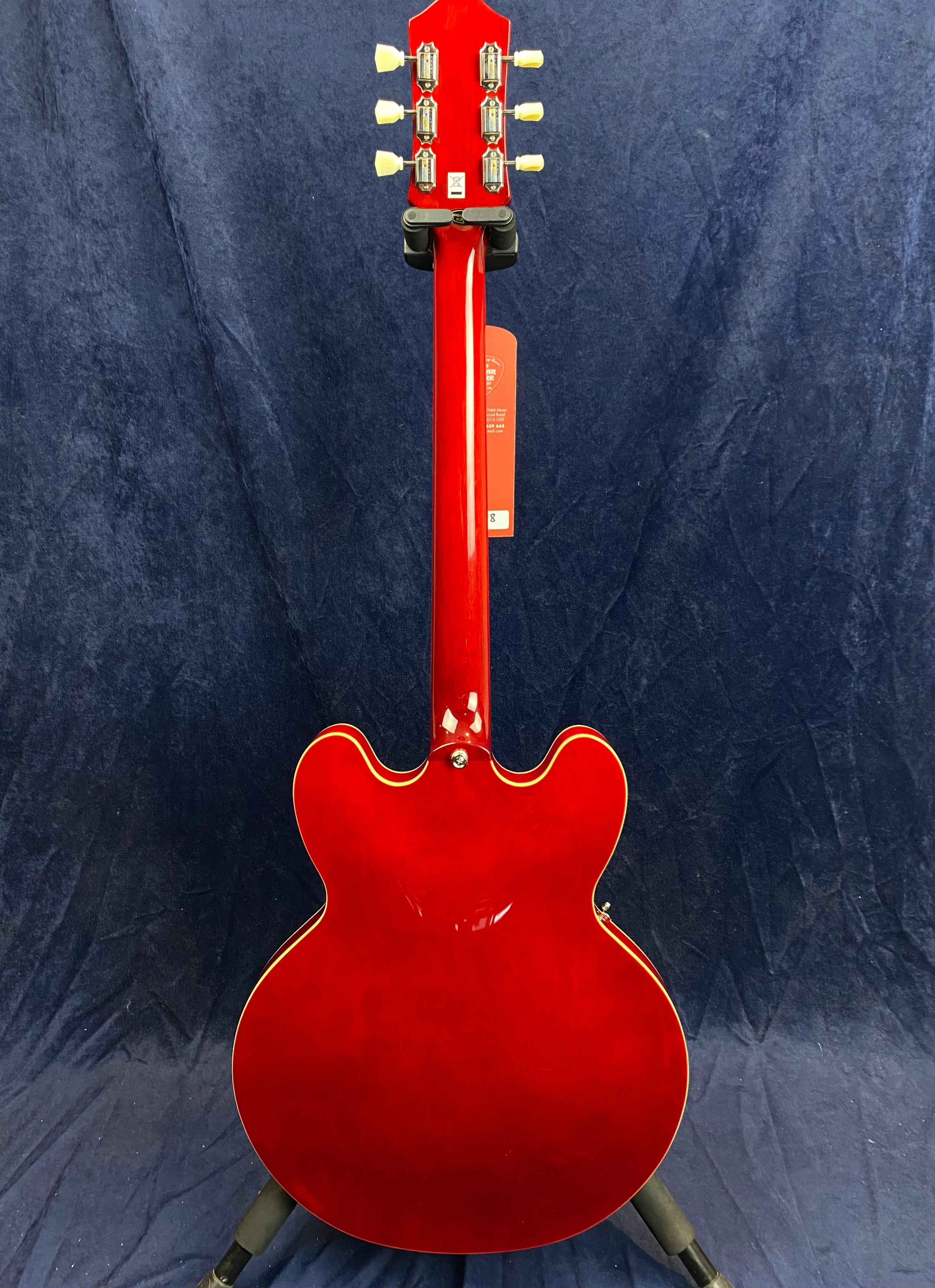 Bright red electric guitar with a semi-hollow, double-cutaway body and cream binding, shown from the back against a dark blue background.
