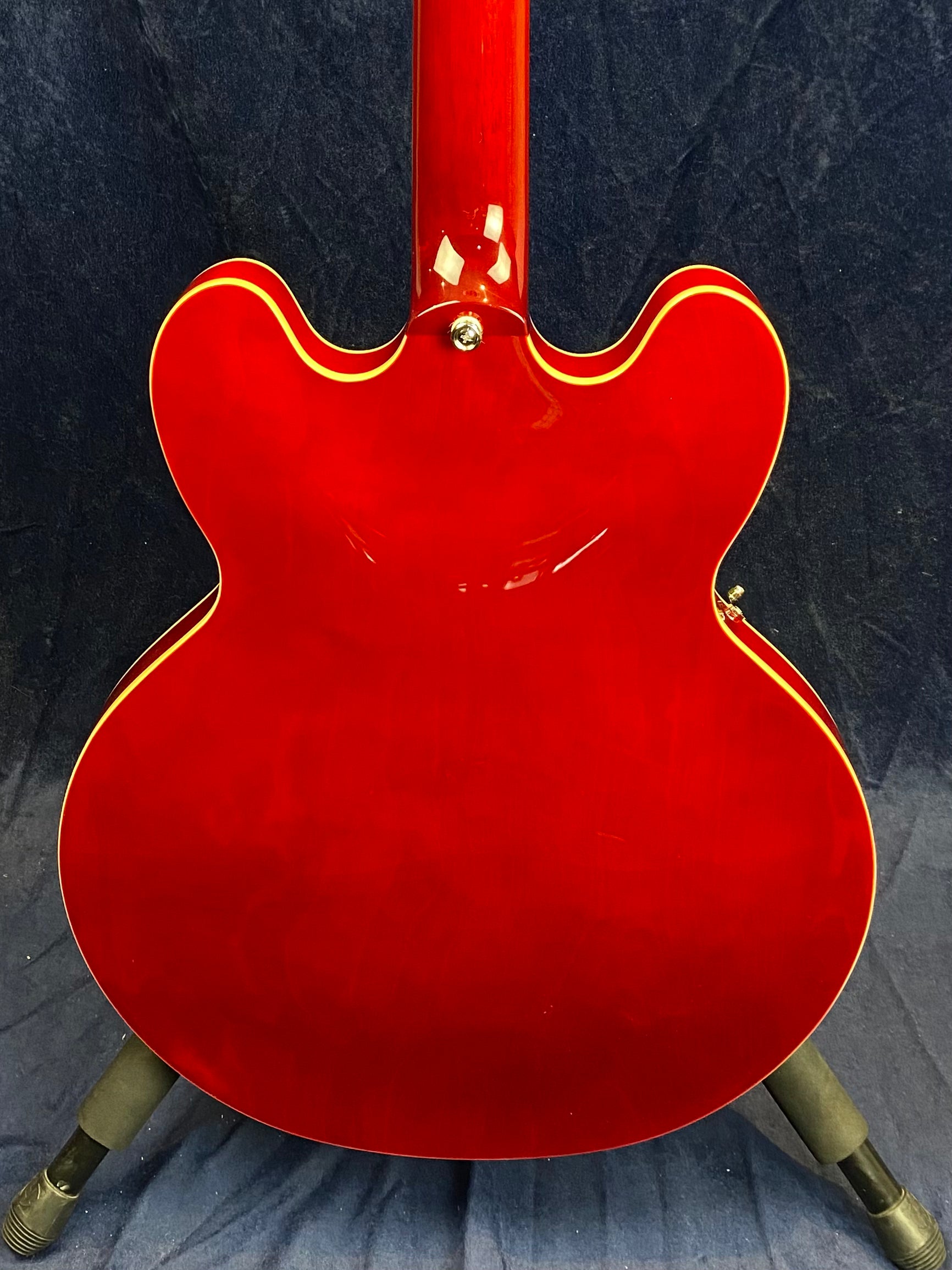 Back view of a glossy red electric guitar with cream binding, double cutaway body, and visible neck joint, standing against a dark background.