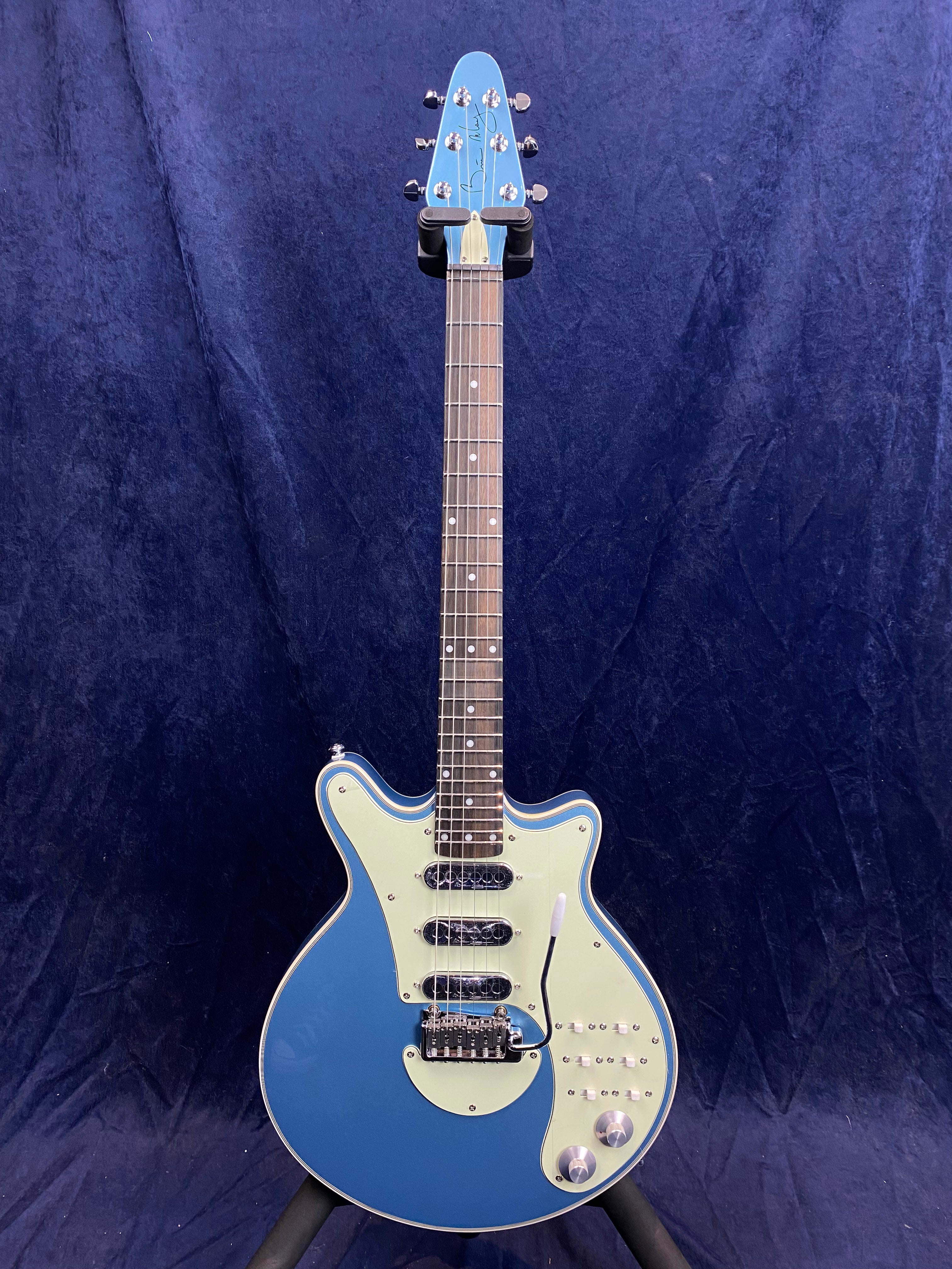 Blue electric guitar with a light green pickguard, three single-coil pickups, two control knobs, multiple switches, and a vibrato bar.