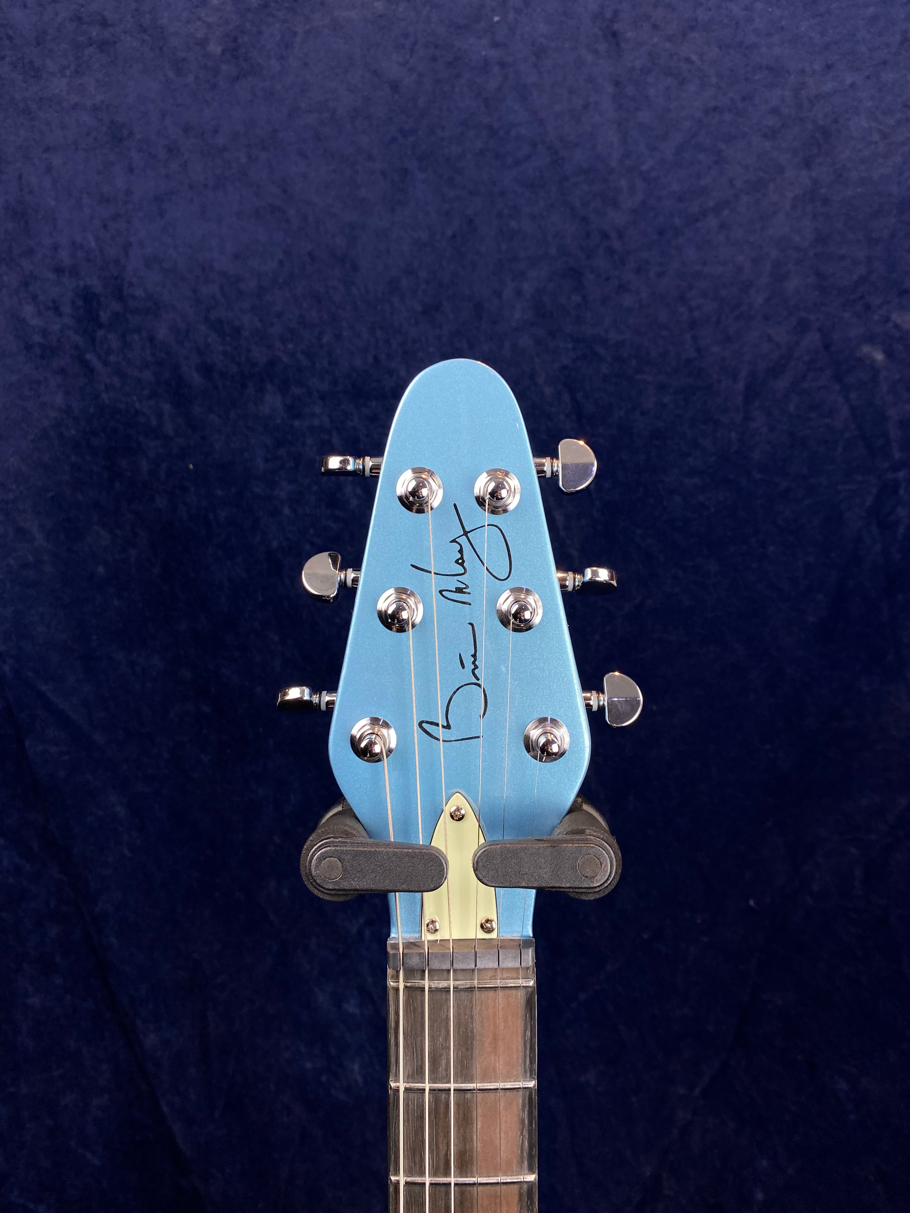 Light blue electric guitar headstock with six chrome tuning pegs, dark fretboard, and a signature printed in black on the front.