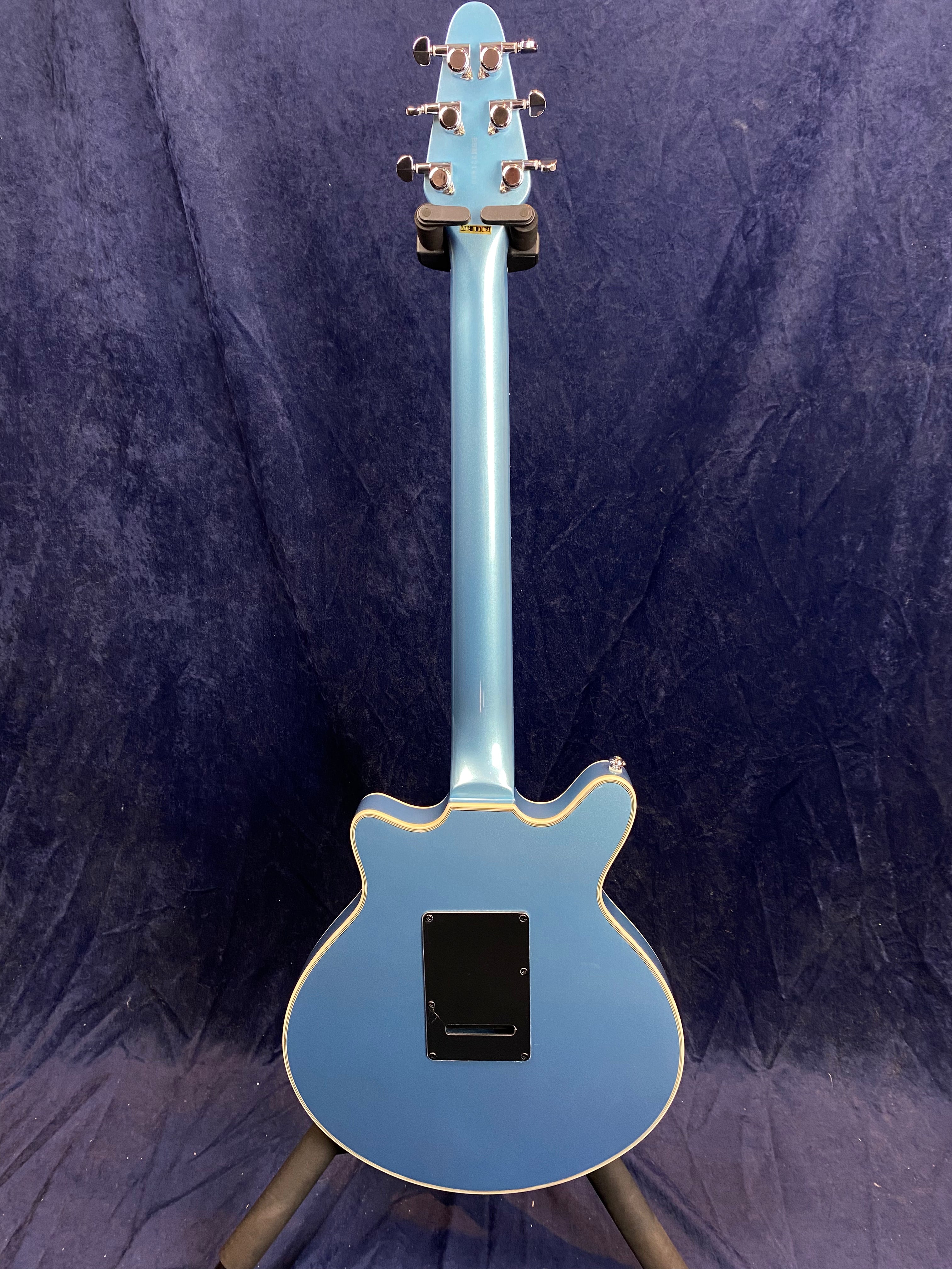 A blue electric guitar seen from the back, featuring a double-cutaway body and a rectangular black electronics cover near the center.
