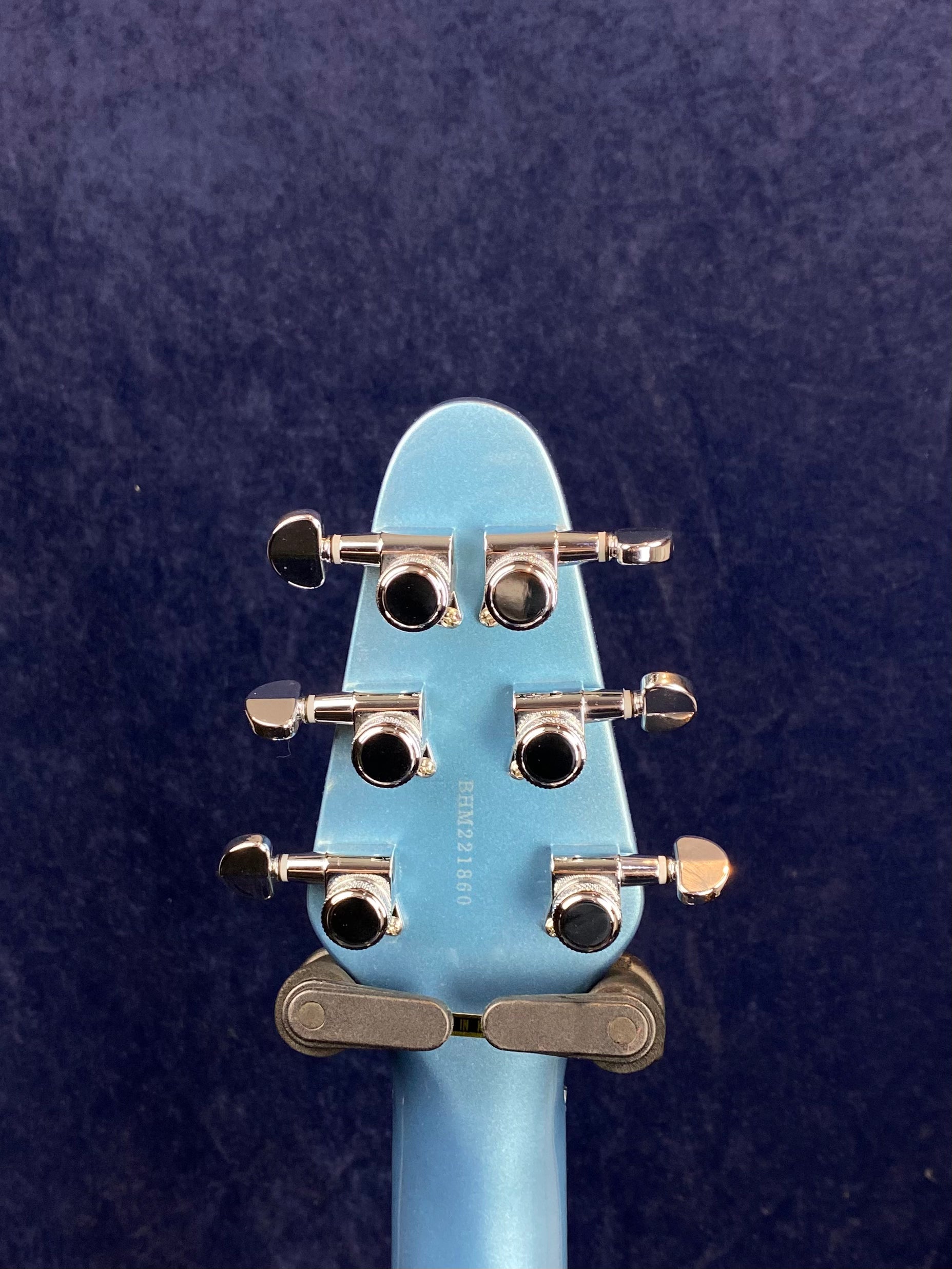 Light blue electric guitar headstock with six chrome tuning pegs, three on each side, against a dark blue background.