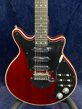 Electric guitar with a deep red body, black pickguard, three chrome pickups, multiple switches, knobs, and a white tremolo arm.