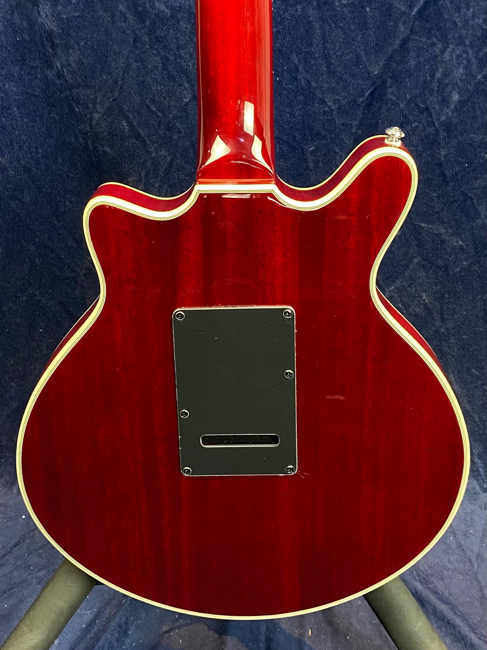 Back of a red electric guitar with cream binding, dual cutaways, and a rectangular black plastic cover plate at the center.