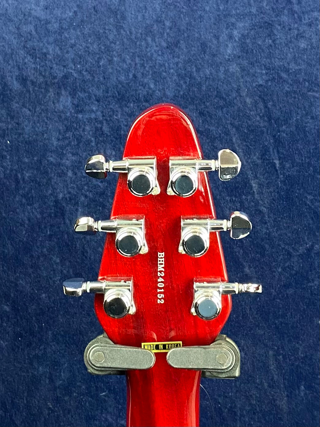 Red electric guitar headstock with six silver tuning pegs, serial number BHM240152, and a "Made in Korea" label on the back.