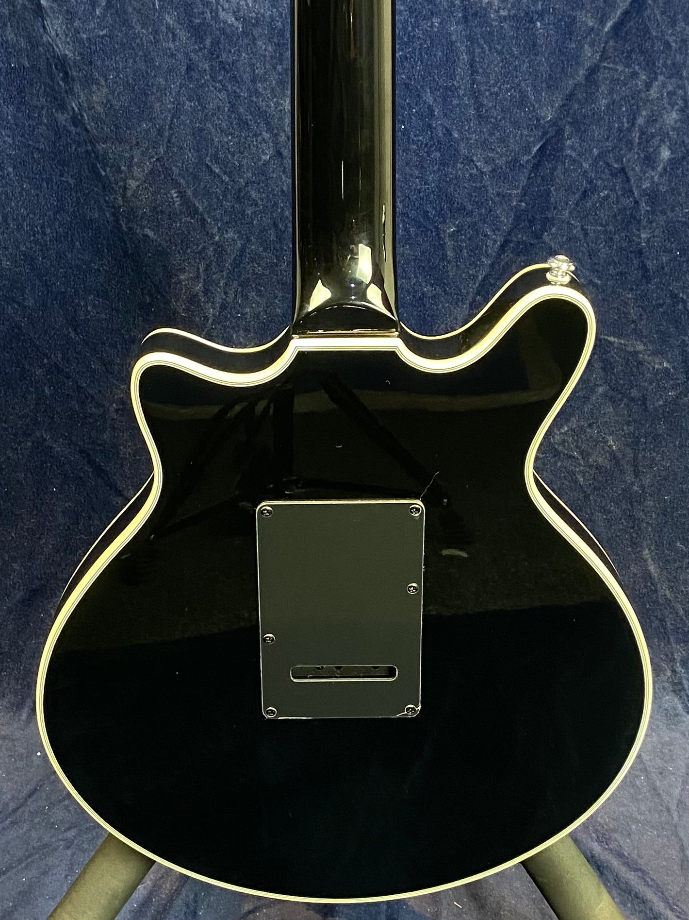 Back view of a black electric guitar with cream-colored trim and a rectangular electronics cover plate in the center of the body.