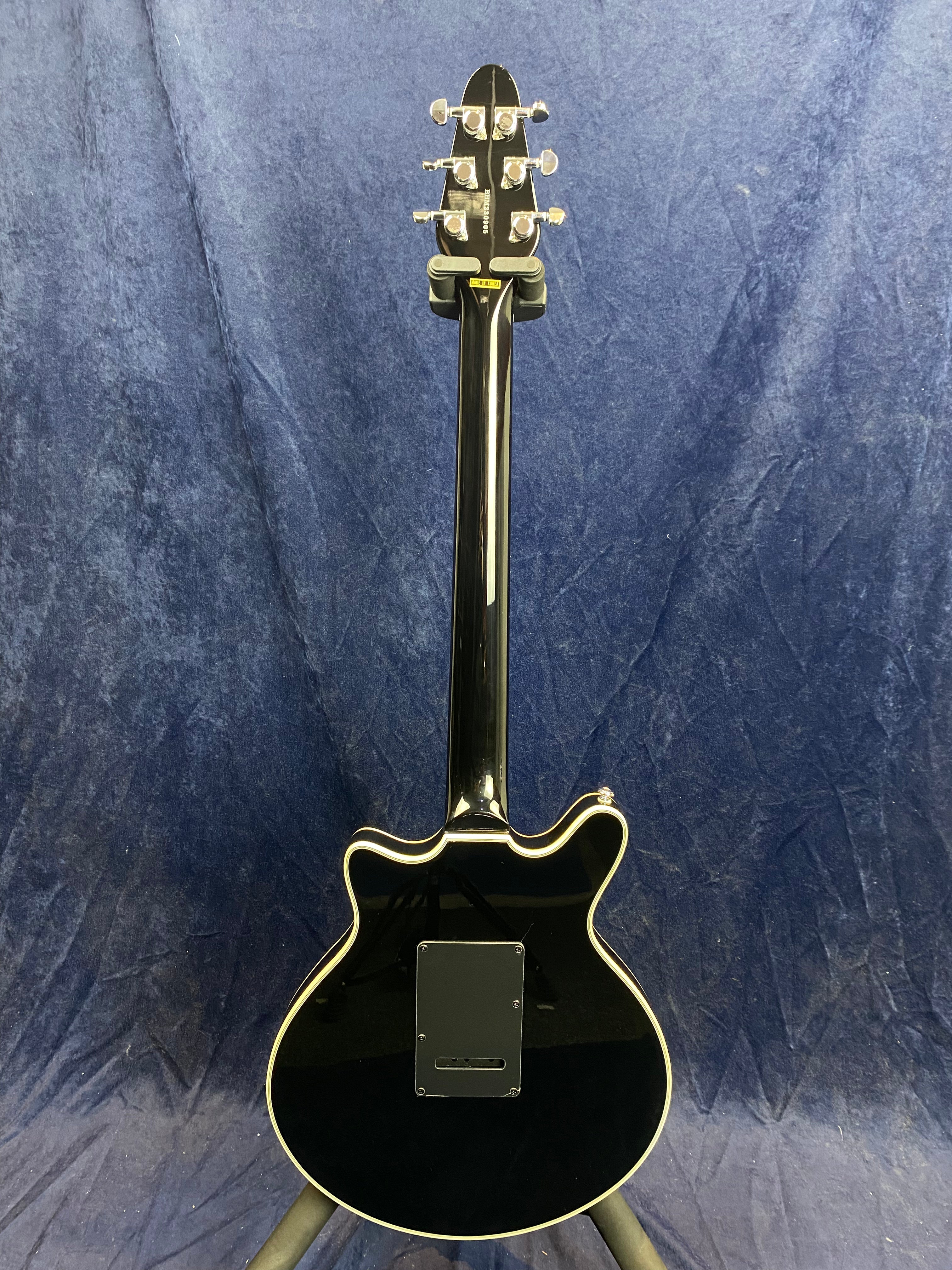 Glossy black electric guitar shown from the back; features silver tuning pegs and a rectangular backplate on the body.