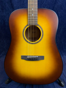 Dreadnought acoustic guitar with a sunburst finish, six steel strings, round sound hole, and dark wood bridge against a dark blue background.