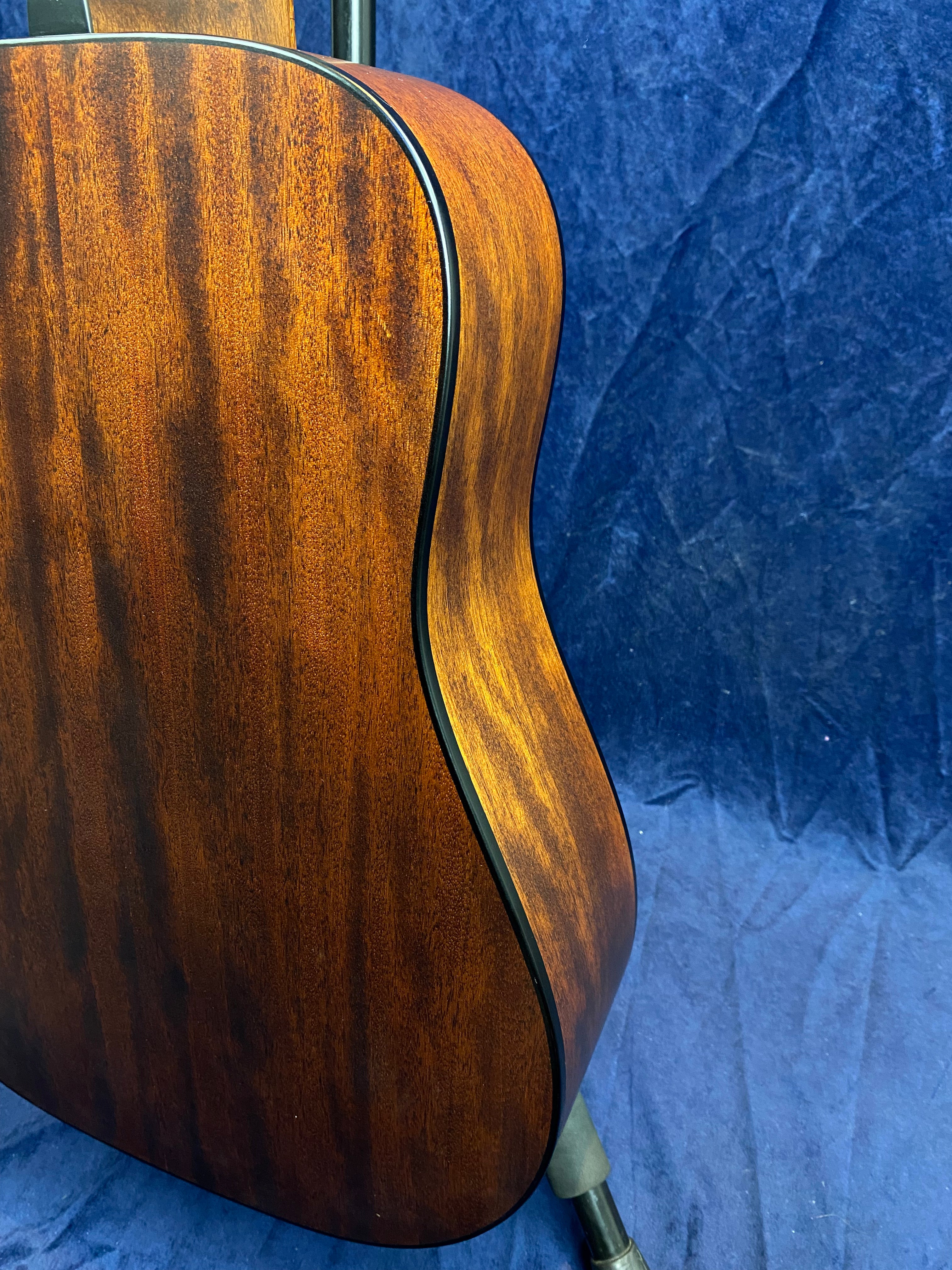 Curved wooden side and back of an acoustic guitar with a rich, dark brown grain finish, set against a deep blue textured background.