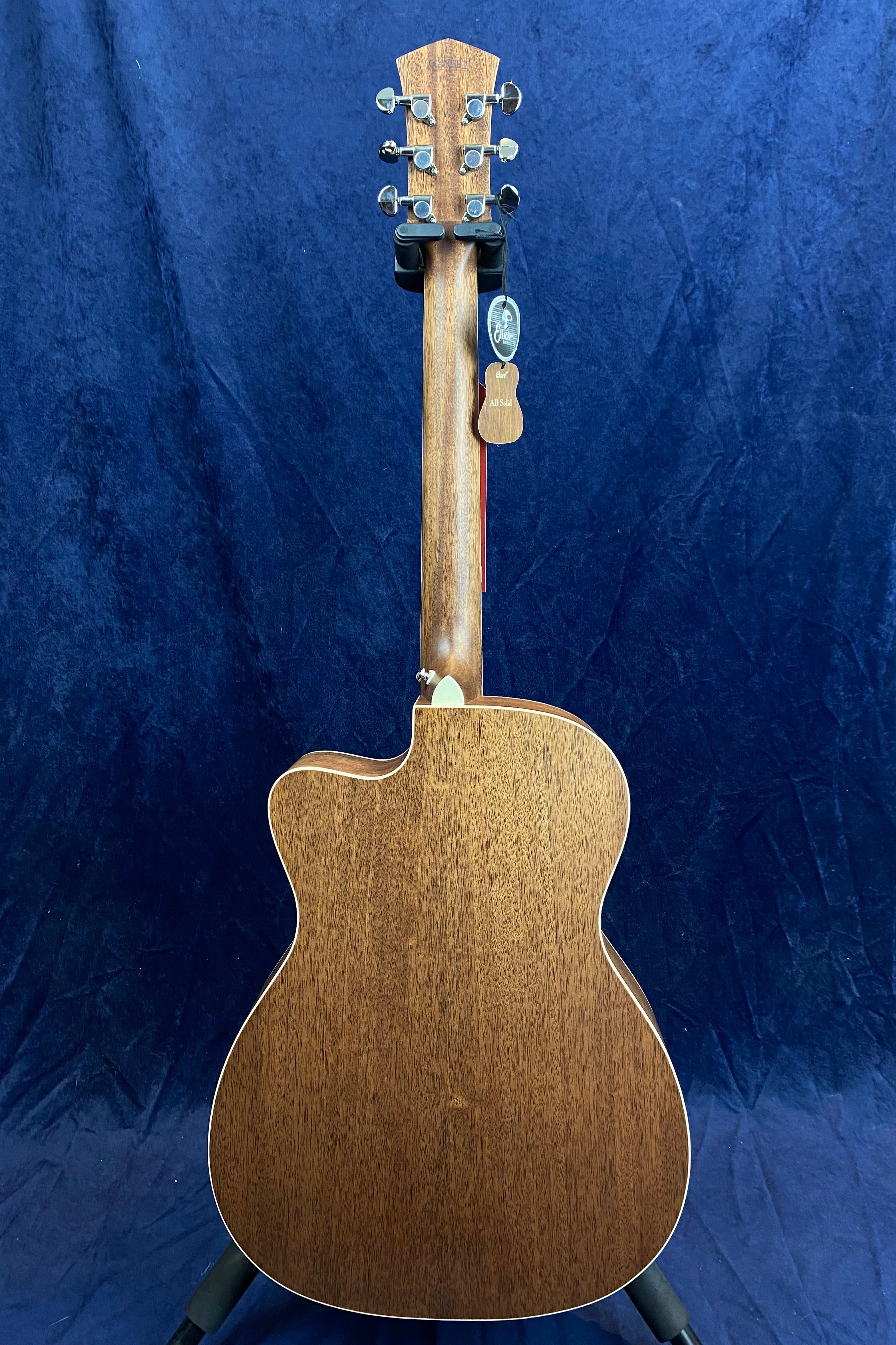 Brown acoustic guitar shown from the back, cutaway body, metal tuning pegs, and a product tag hanging from the headstock.