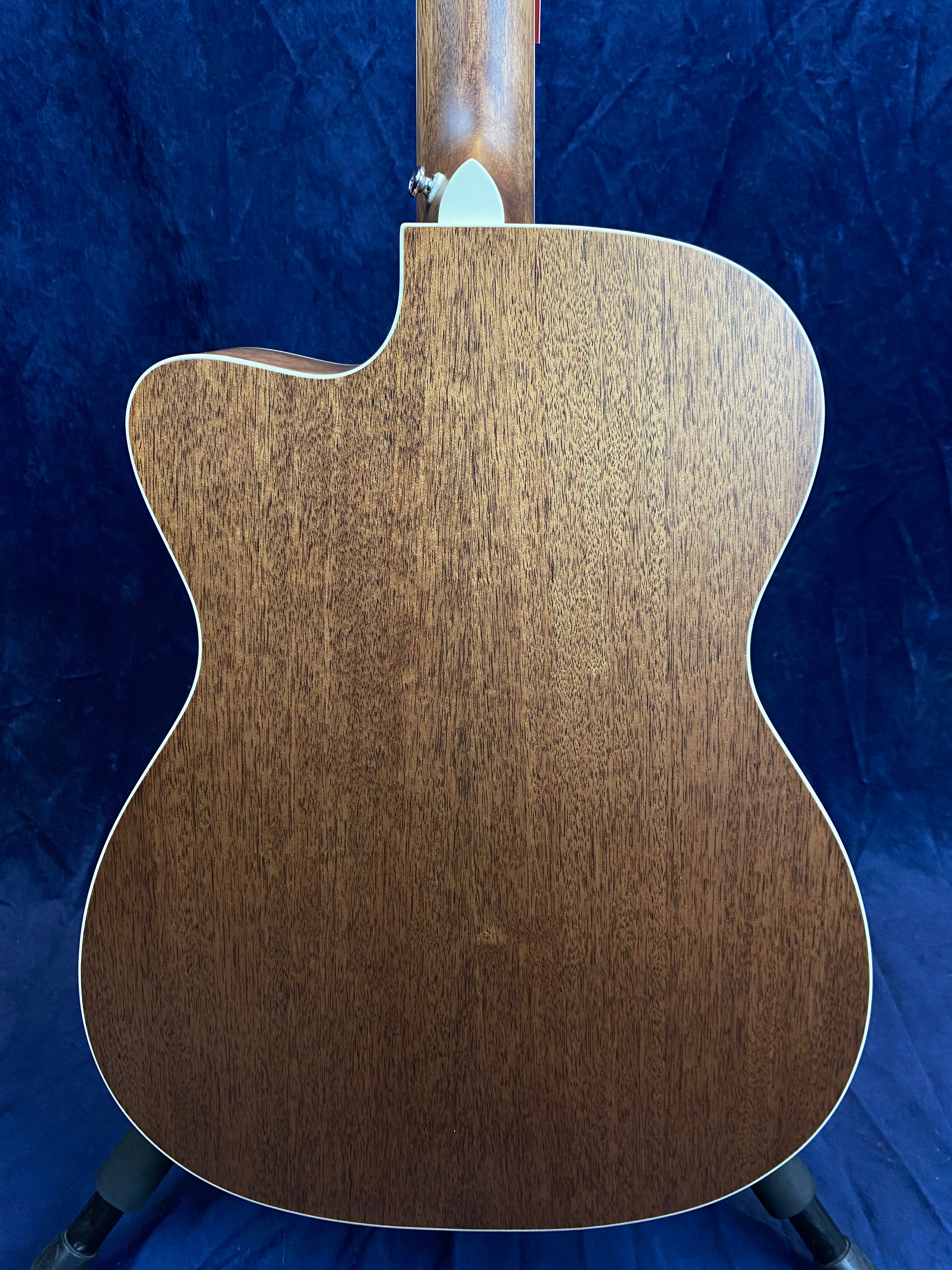 Back view of an acoustic guitar showing natural brown wood grain with cream-colored trim, cutaway body shape, and part of the neck visible.