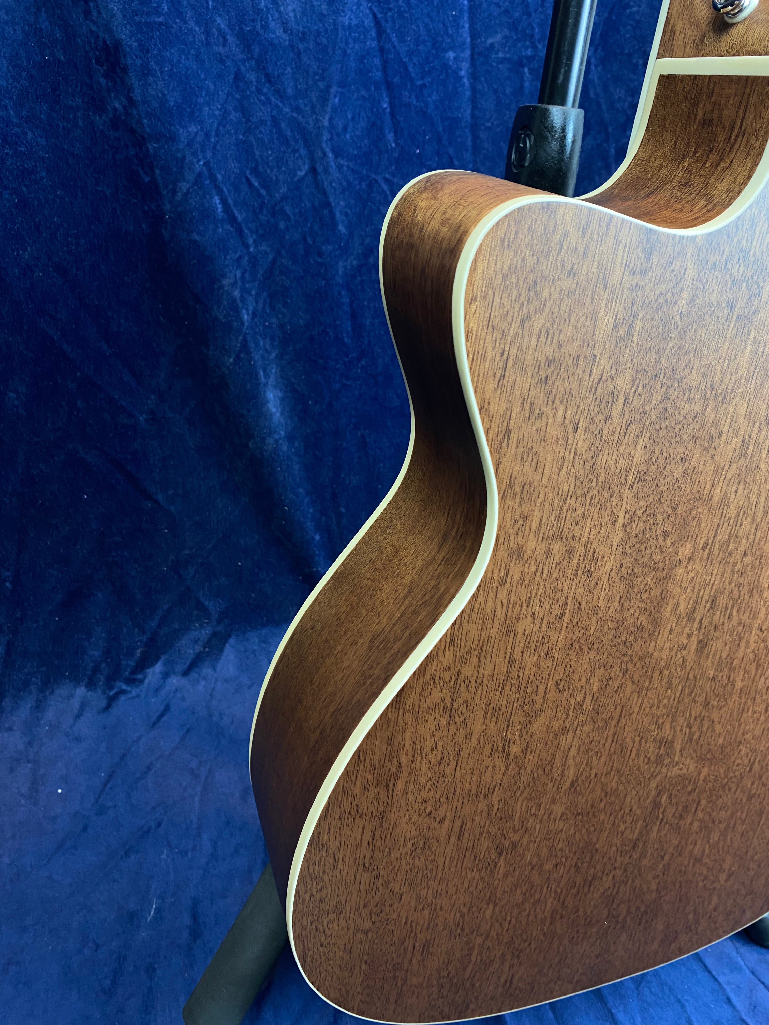 Brown acoustic guitar body with cream binding, shown from the back against a deep blue textured background. No visible neck or strings.