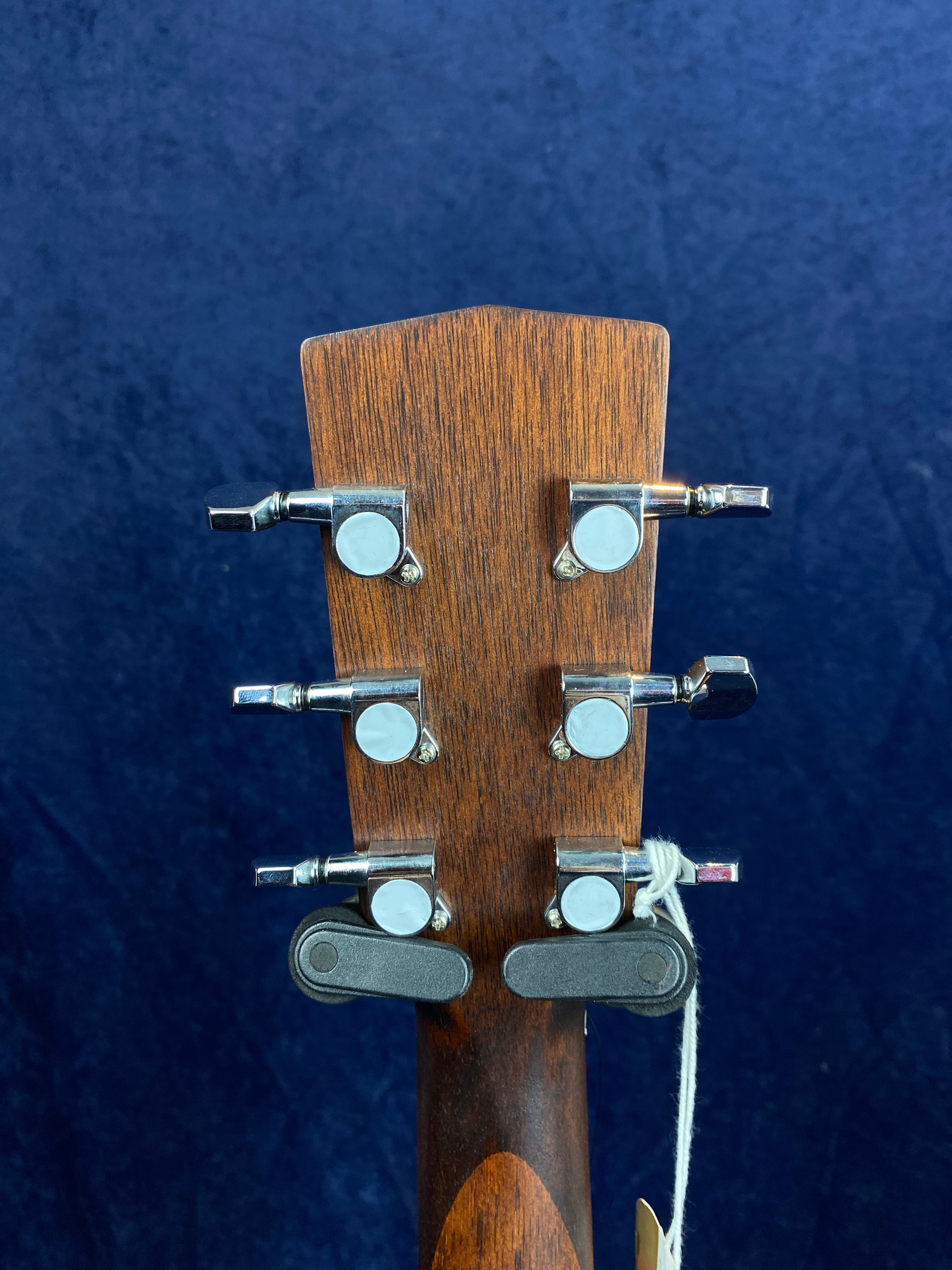 Six silver tuning pegs on a wooden acoustic guitar headstock; two black capo-style accessories attached and white string tied to one peg.