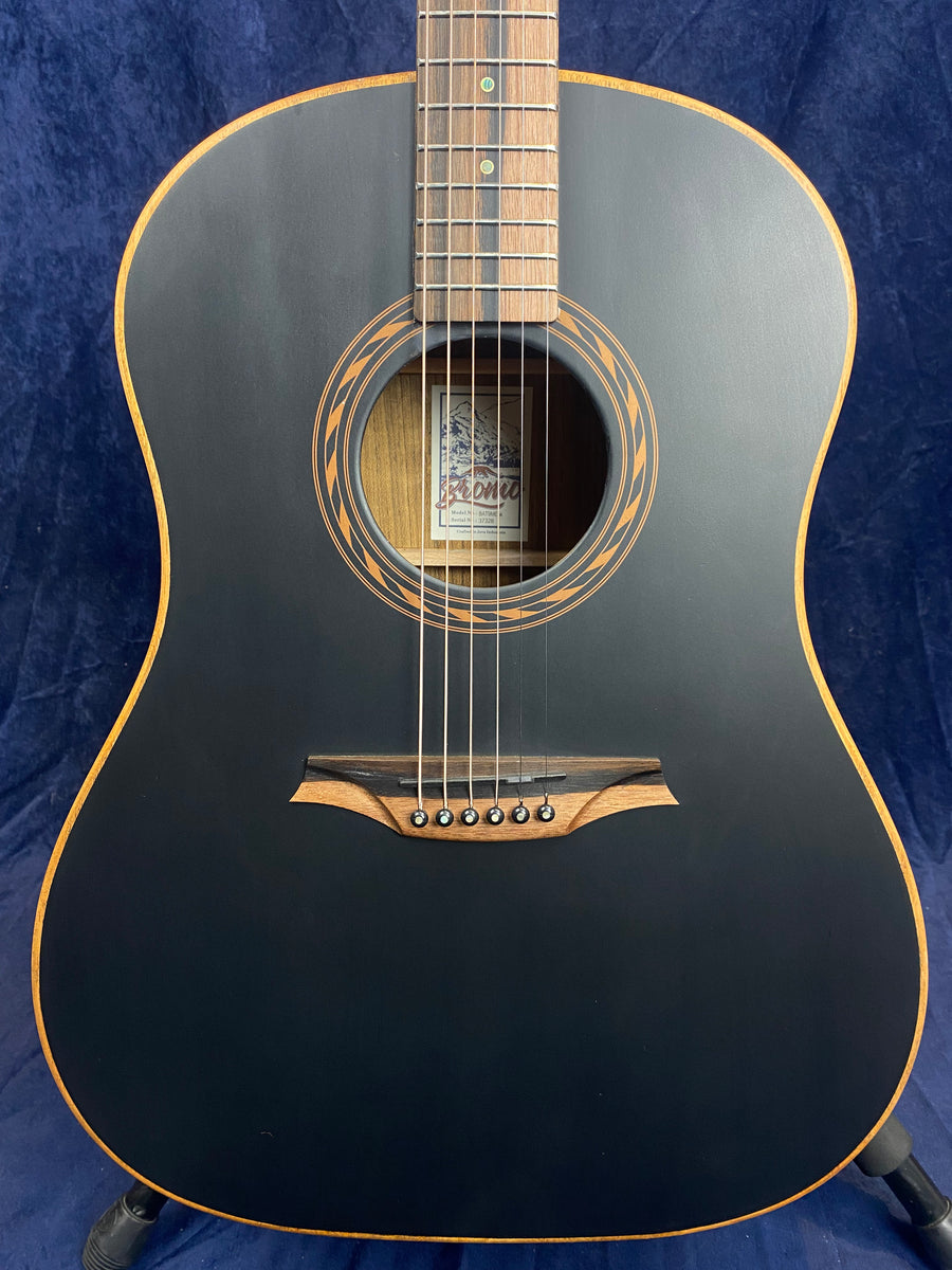 Matte black acoustic guitar with light wood trim, a decorative rosette around the sound hole, and a uniquely shaped two-tone wooden bridge.