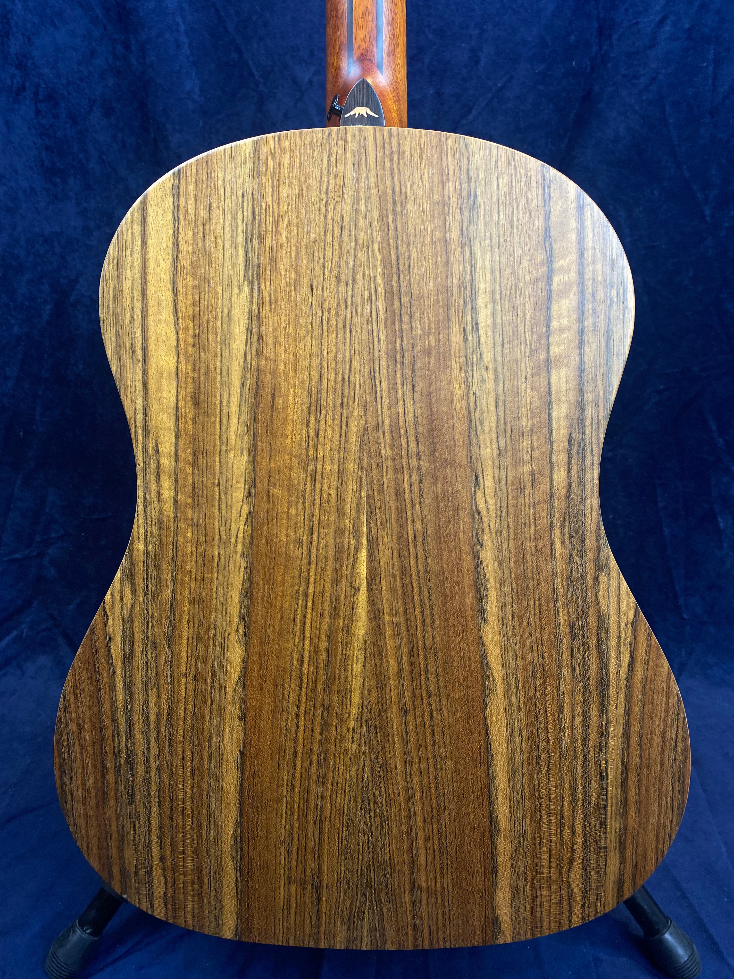 The back of an acoustic guitar made of wood with a natural finish and vertical dark and light brown grain patterns.