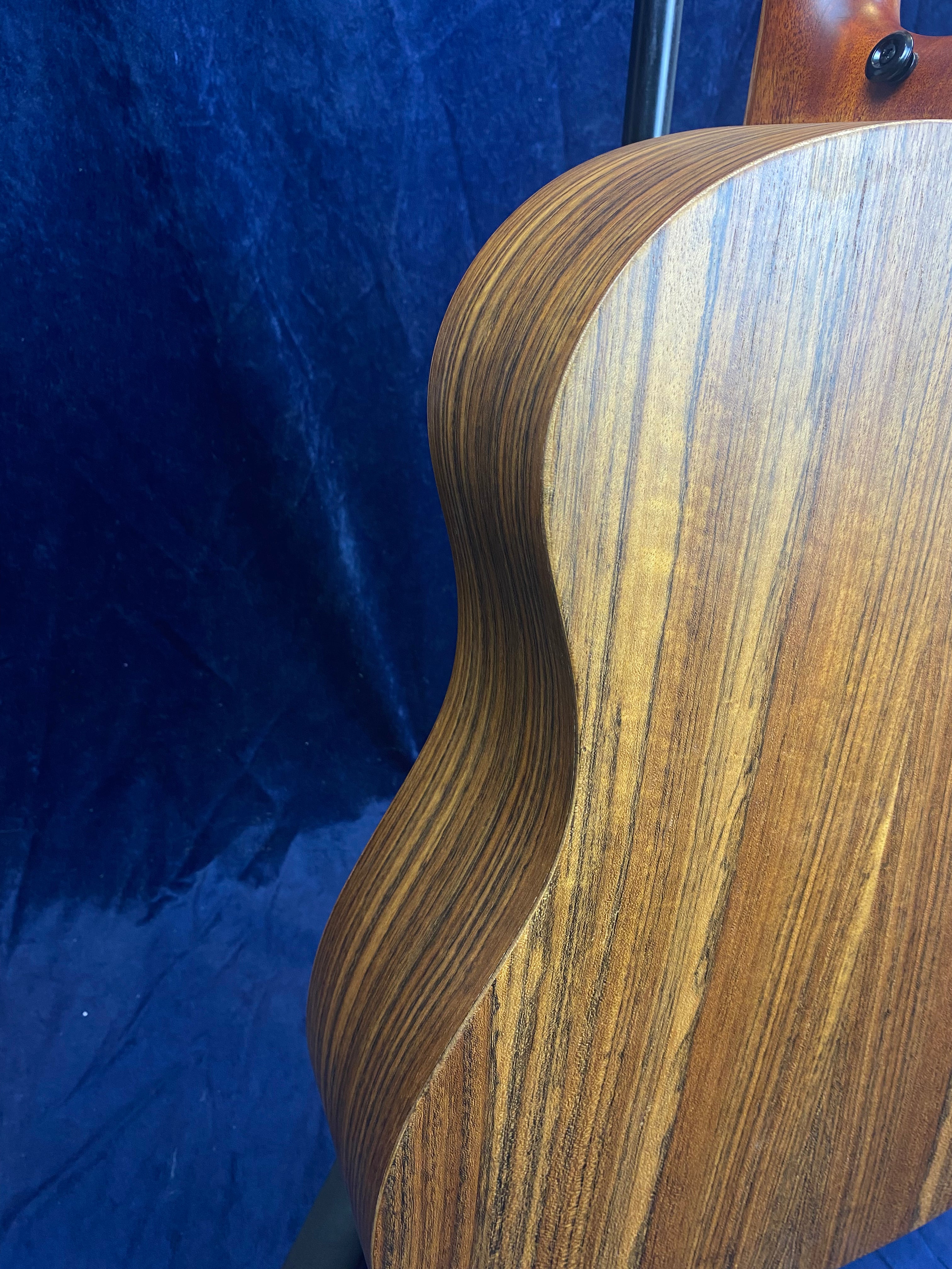 Curved wood grain back and side of an acoustic guitar, showing smooth craftsmanship and natural brown and dark stripe patterns.