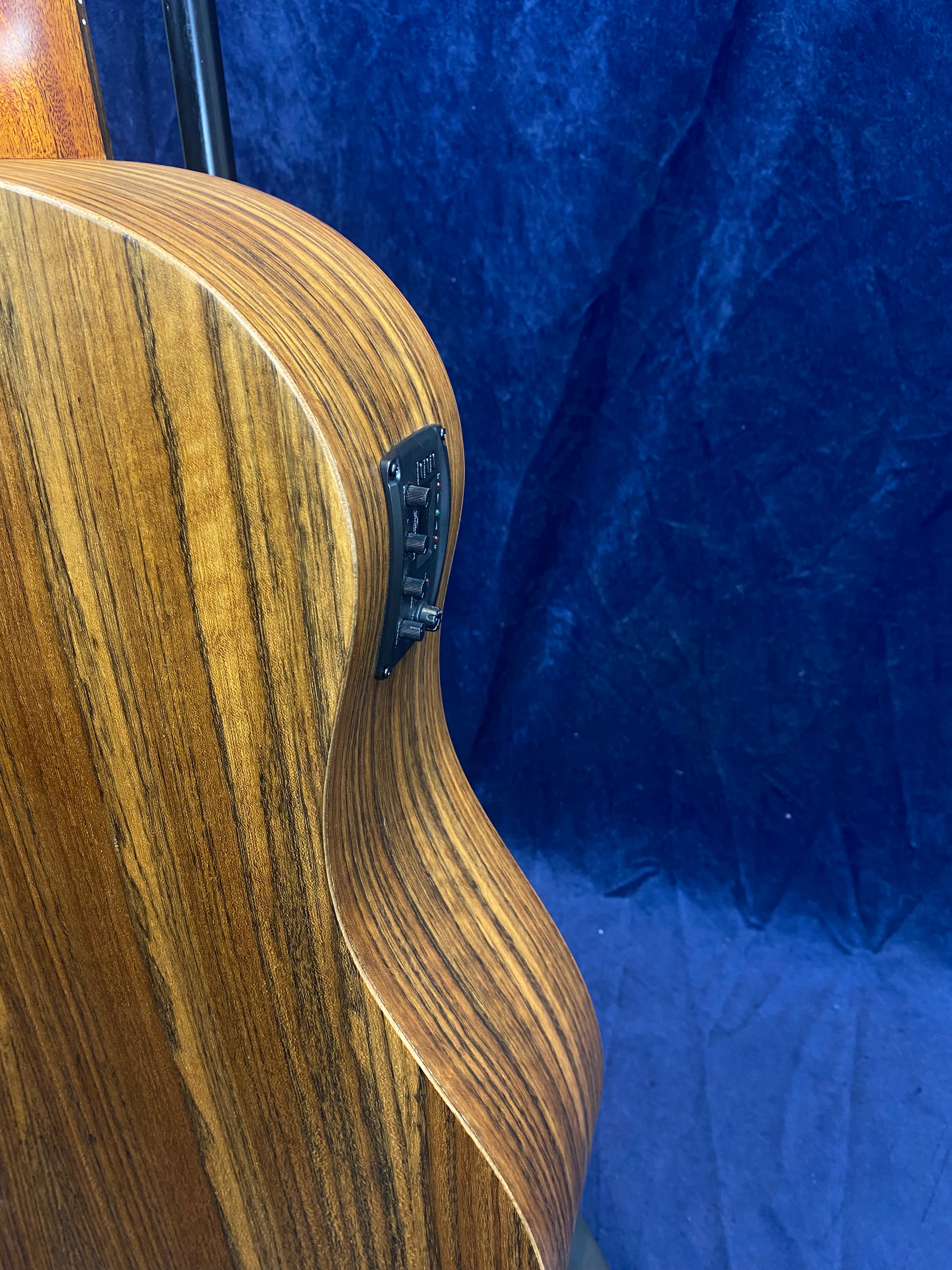 Curved side of an acoustic guitar showing light and dark wood grain with a built-in electronic control panel visible on the side.