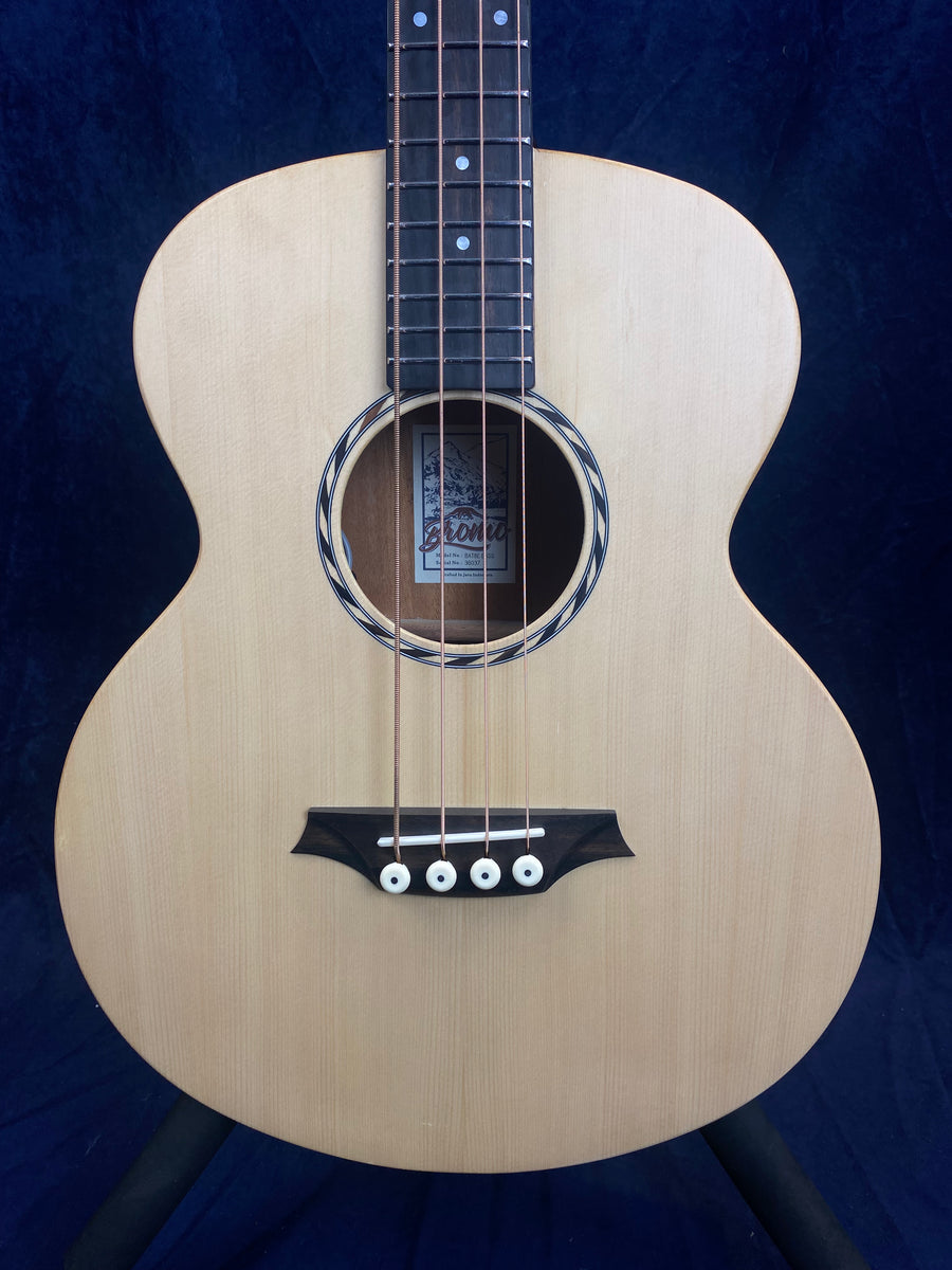 Natural wood acoustic guitar body with four strings, black bridge, white bridge pins, circular sound hole, and dark fingerboard with dot inlays.