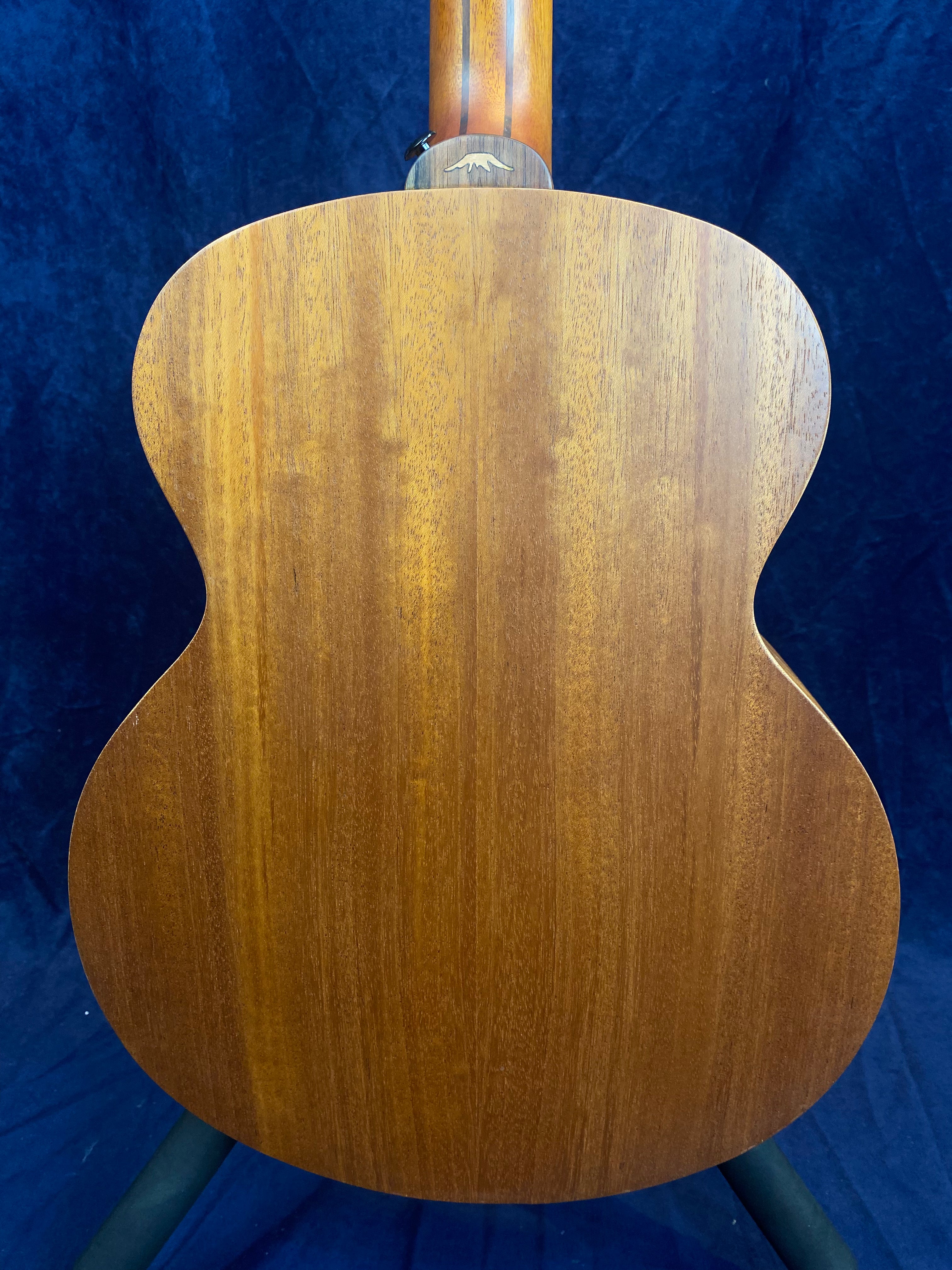 Back view of an acoustic guitar with a smooth, natural wood grain finish, set against a dark blue background.
