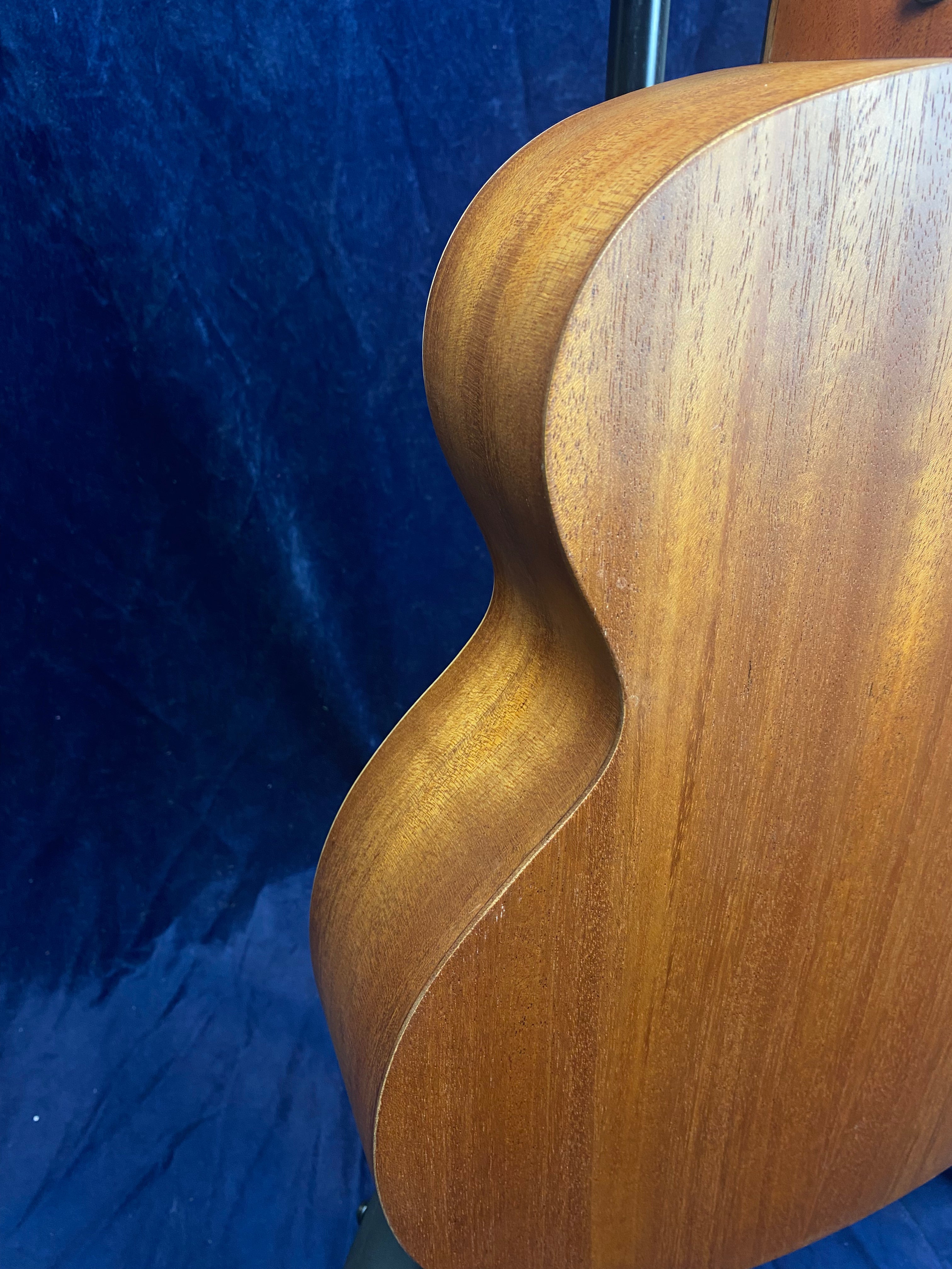 Close-up of the back and side of a wooden acoustic guitar against a dark blue textured background.