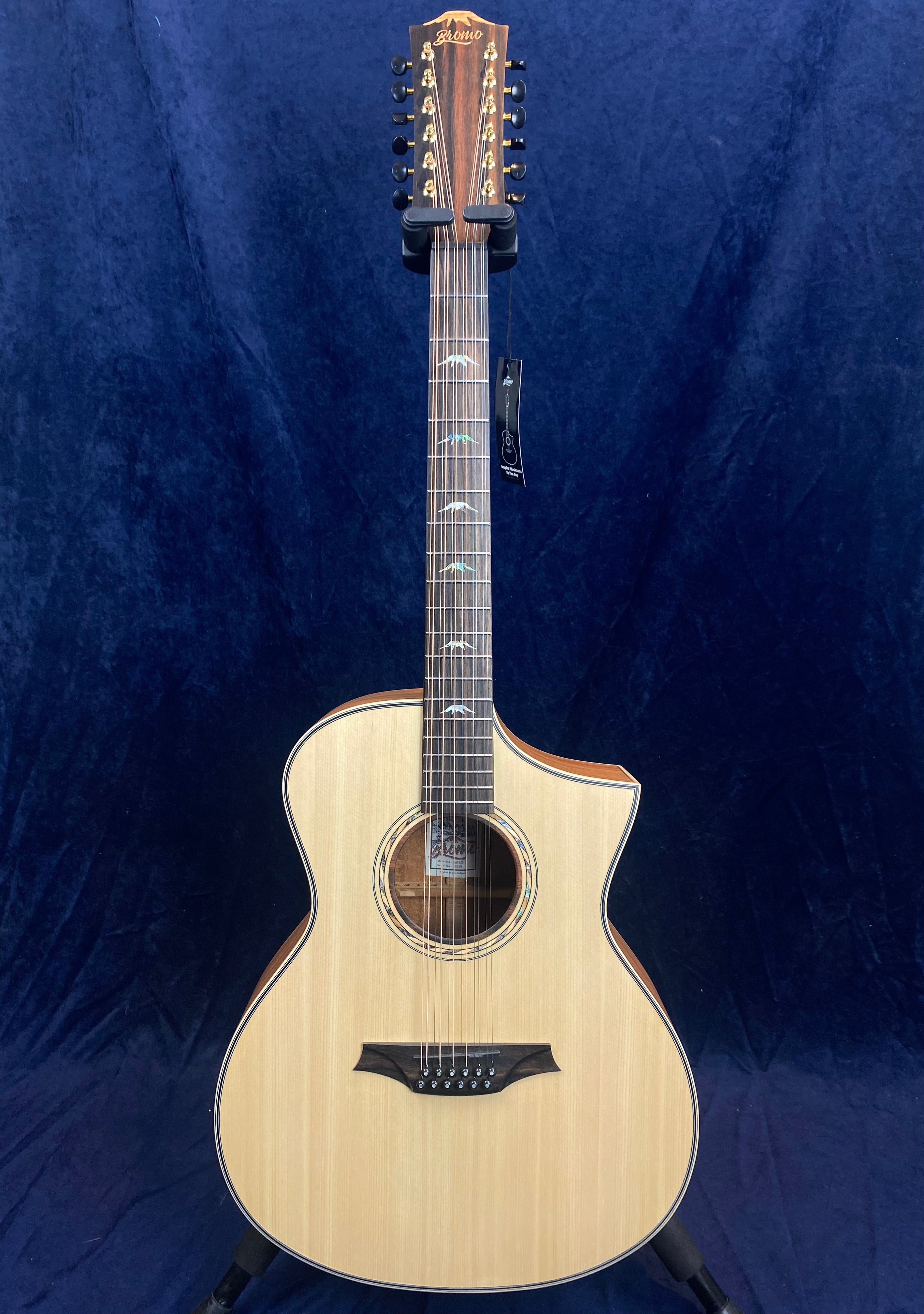 Twelve-string acoustic guitar with a light wood body, cutaway design, dark fretboard, and decorative inlays on the neck, displayed against a dark background.