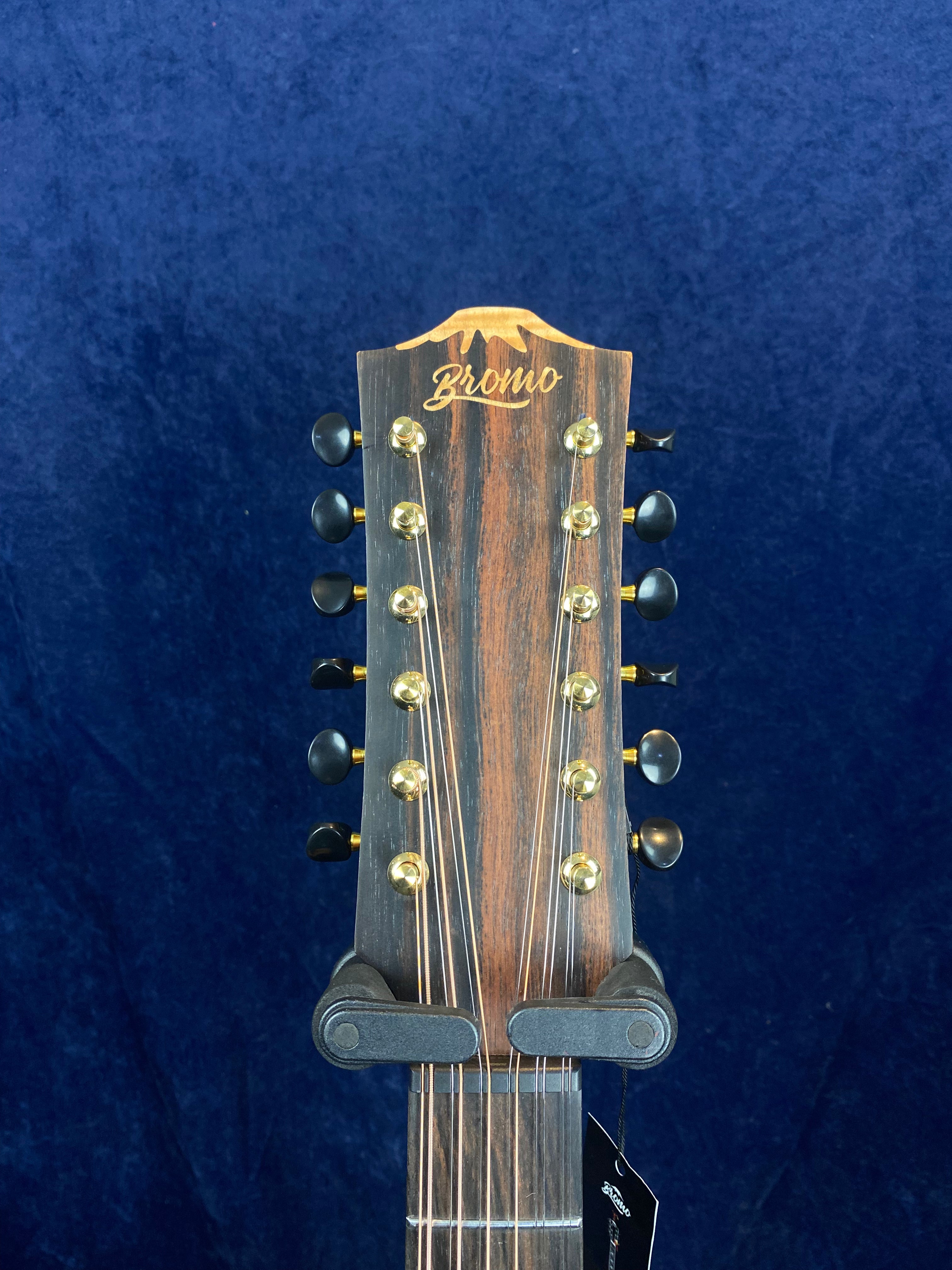 Bromo 12-string acoustic guitar headstock with six gold tuning pegs on each side against a dark blue background.