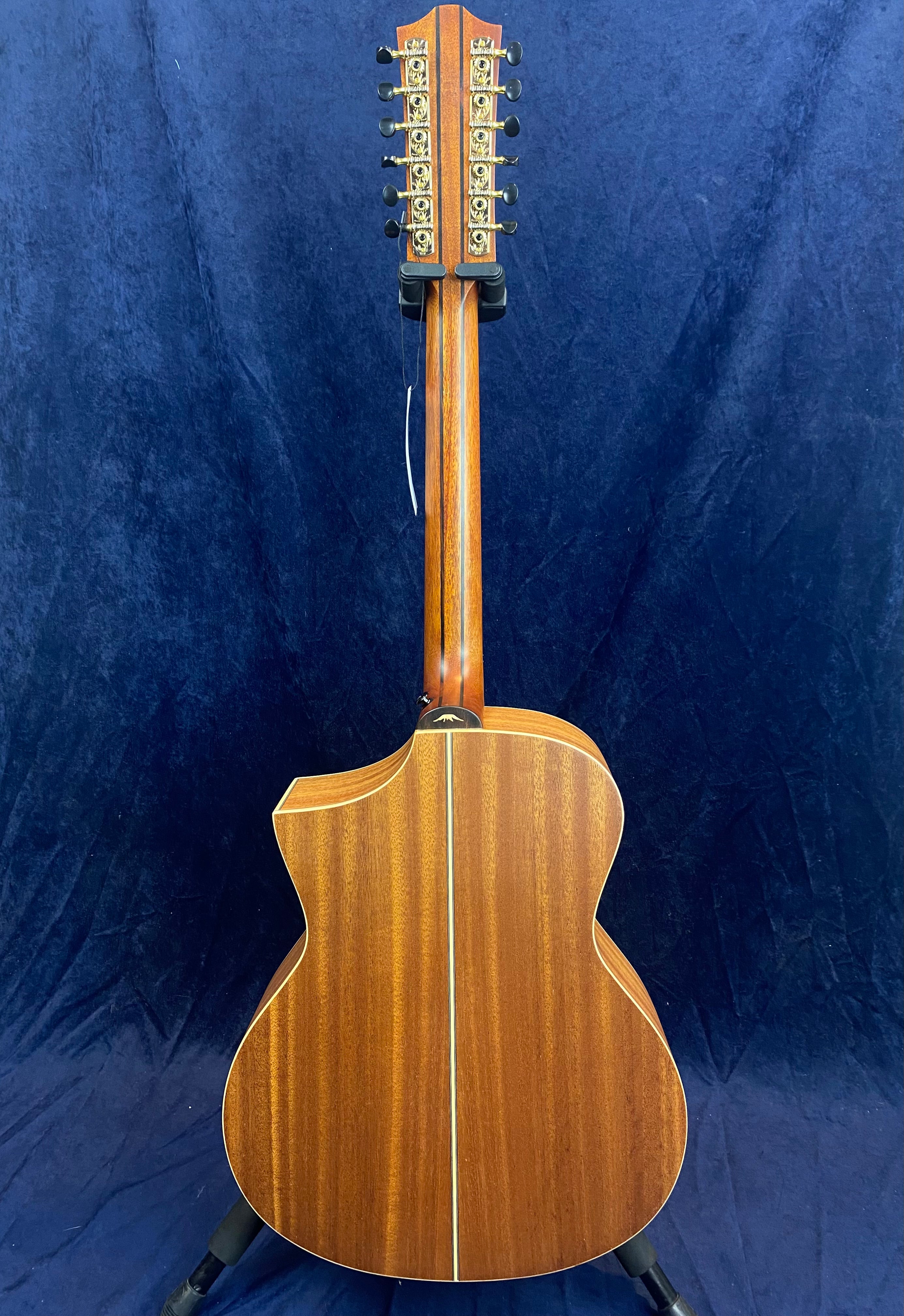 Twelve-string acoustic guitar viewed from the back, showing a rich wood finish, center stripe, cutaway body, and ornate gold tuning machines.