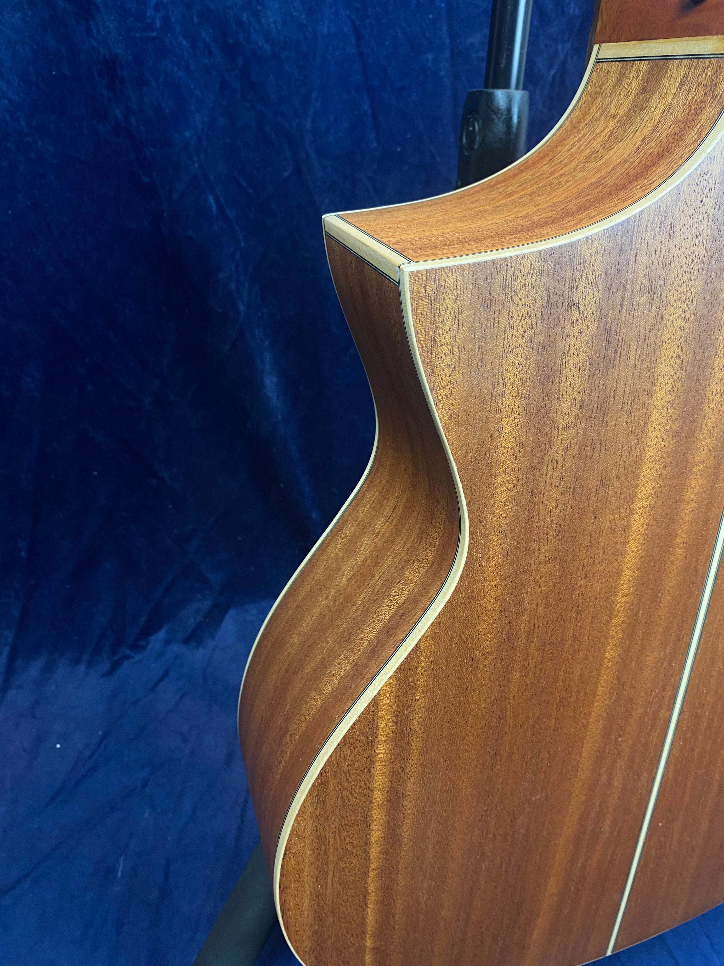 Curved wooden body of an acoustic guitar with a smooth satin finish, cream binding, and a subtle center inlay stripe on the back.