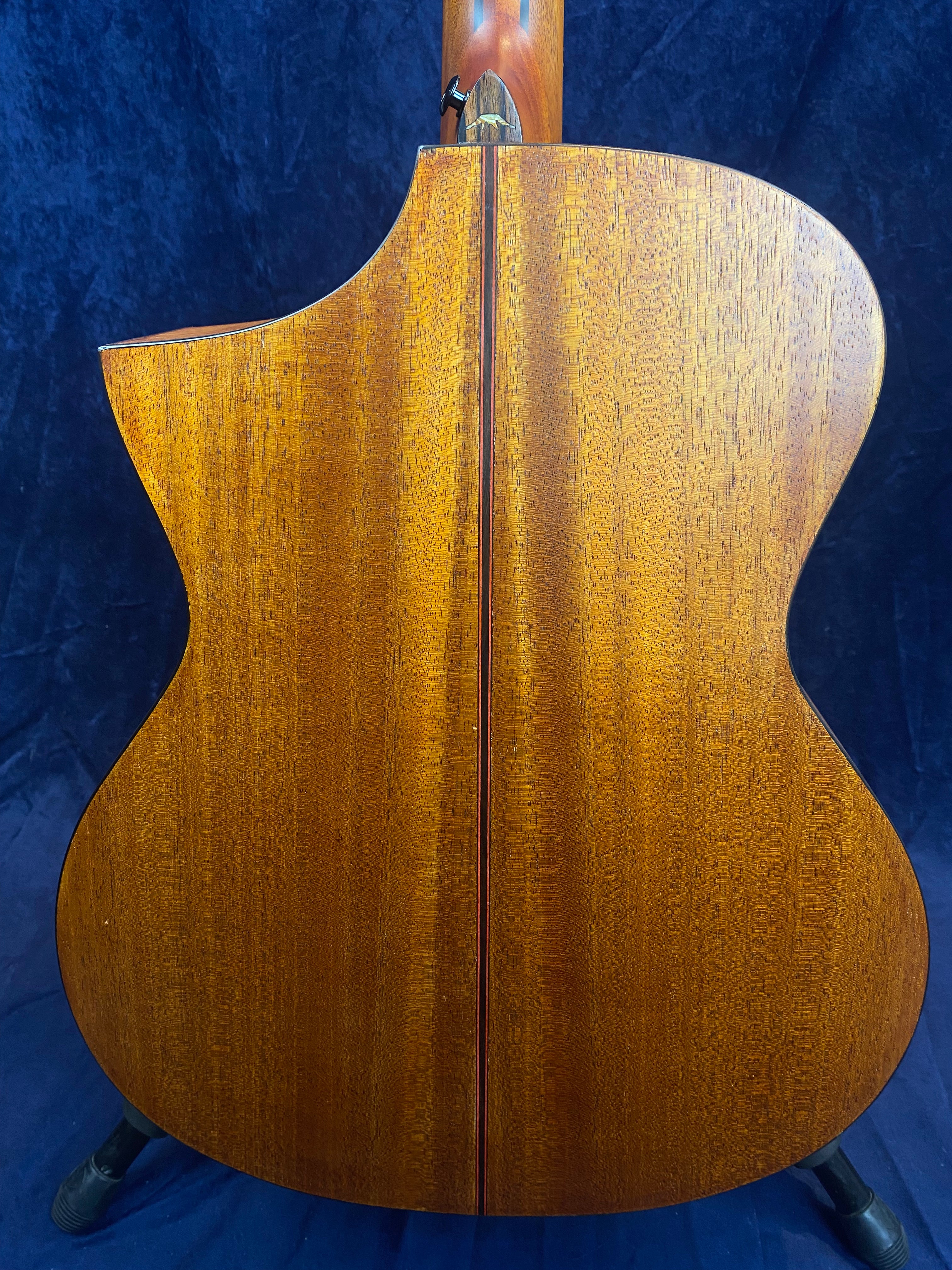 Back of an acoustic guitar with rich brown wood, a visible center seam, and a single cutaway on the left for upper fret access.