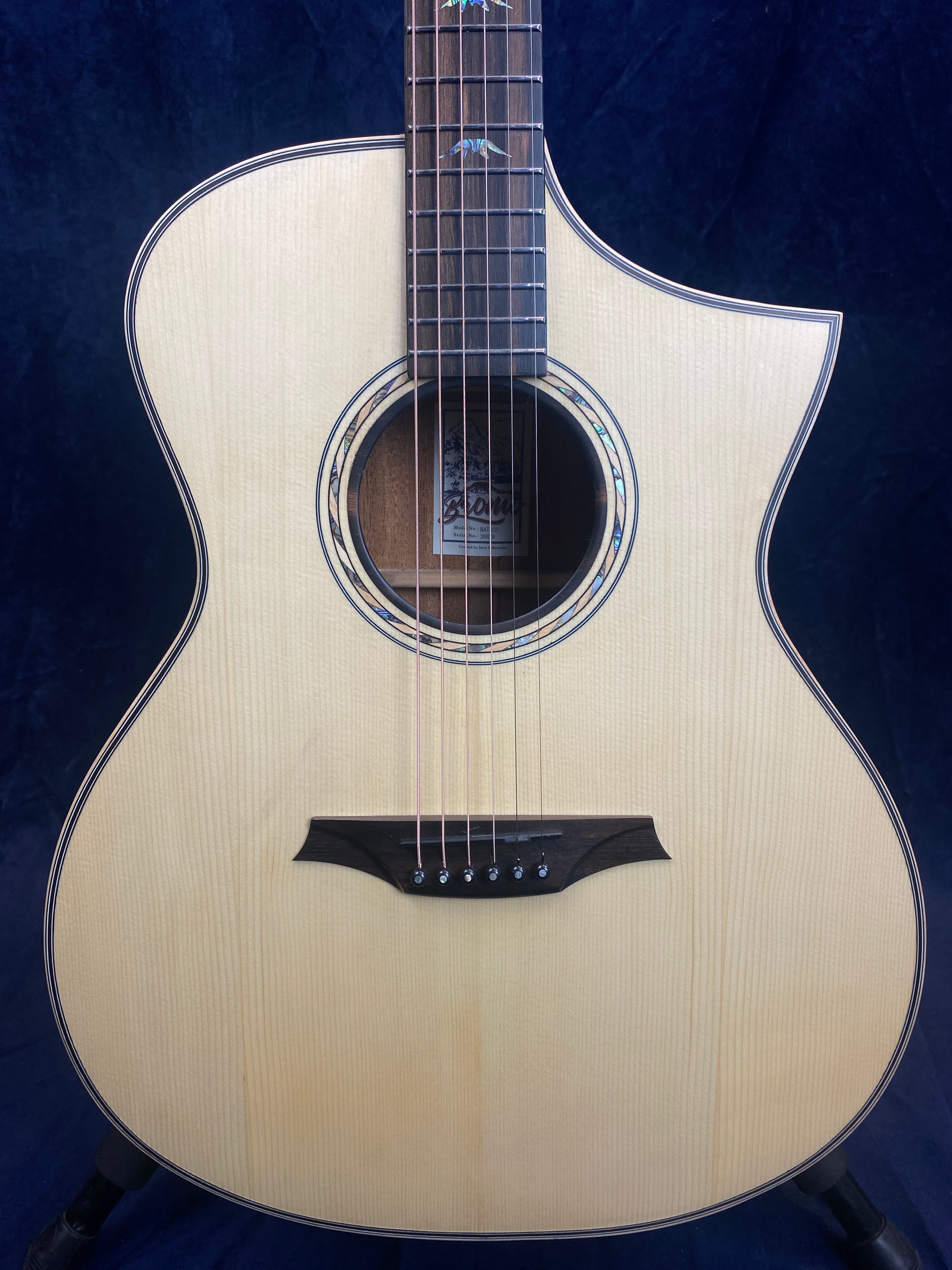 Guitare acoustique à table claire avec pan coupé sur l’épaule, rosace décorative et incrustations colorées sur la touche.