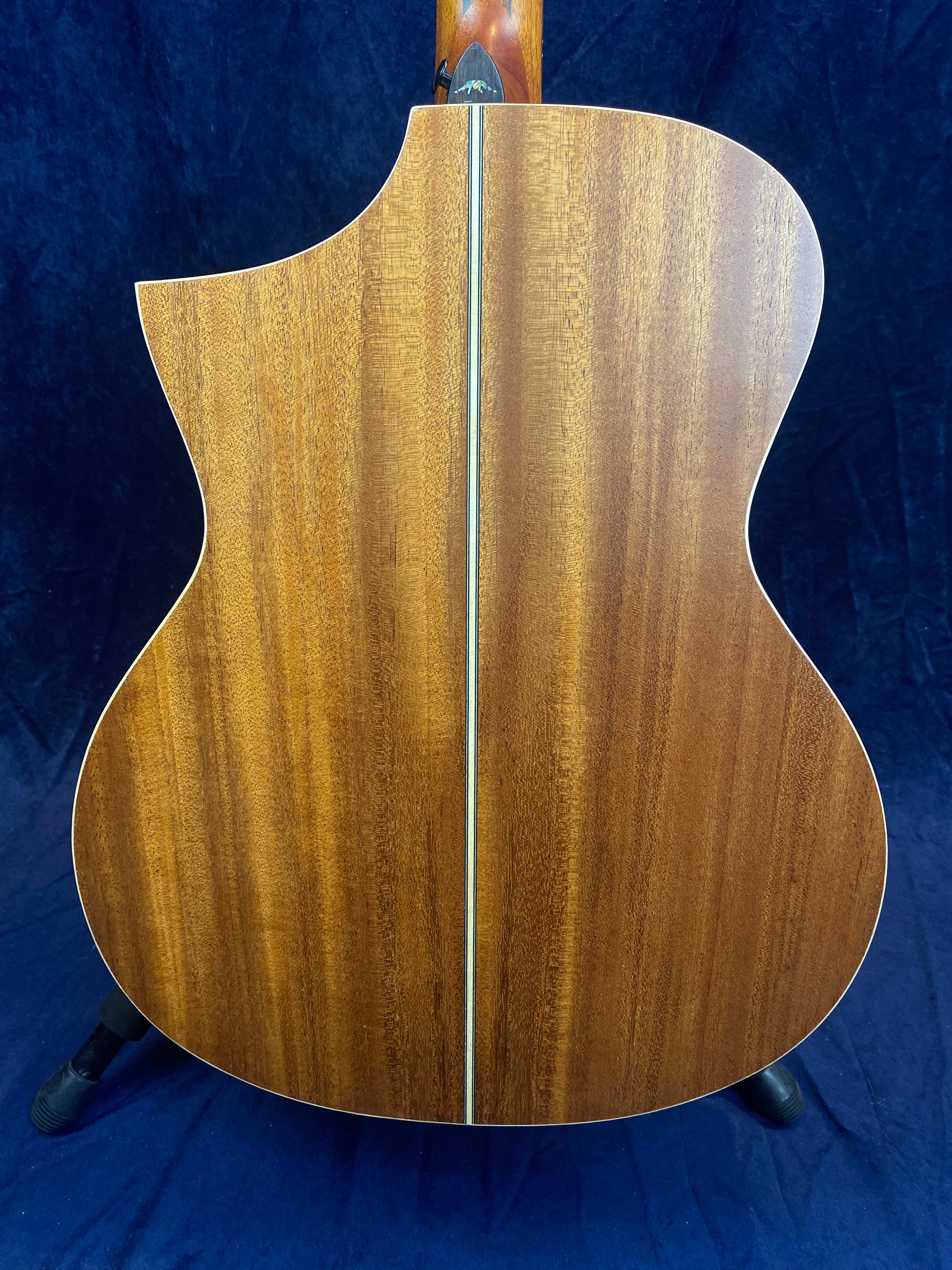 The back of an acoustic guitar with a natural wood finish, a single center inlay, and a cutaway design on the left side.