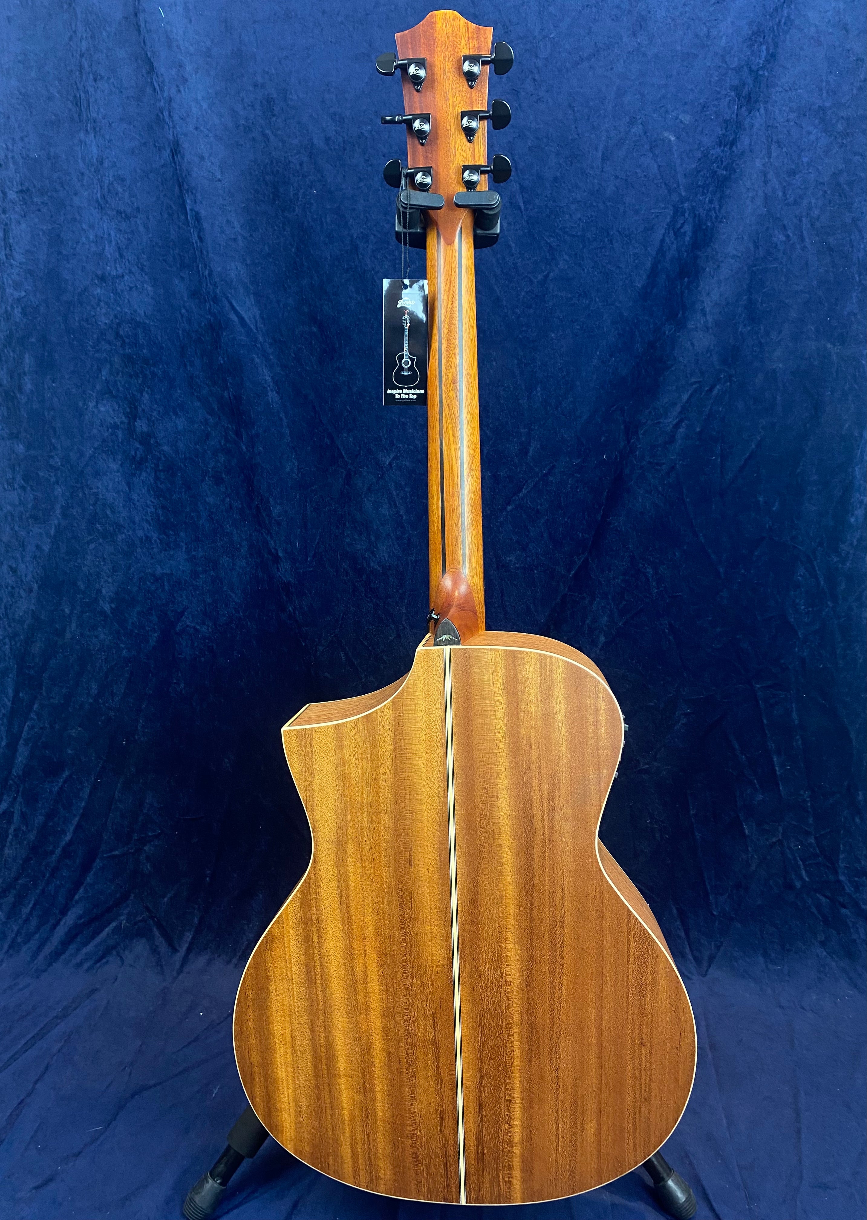 Brown acoustic guitar with a cutaway body, vertical center stripe on the back, and six tuning pegs, shown from the rear against a dark blue background.