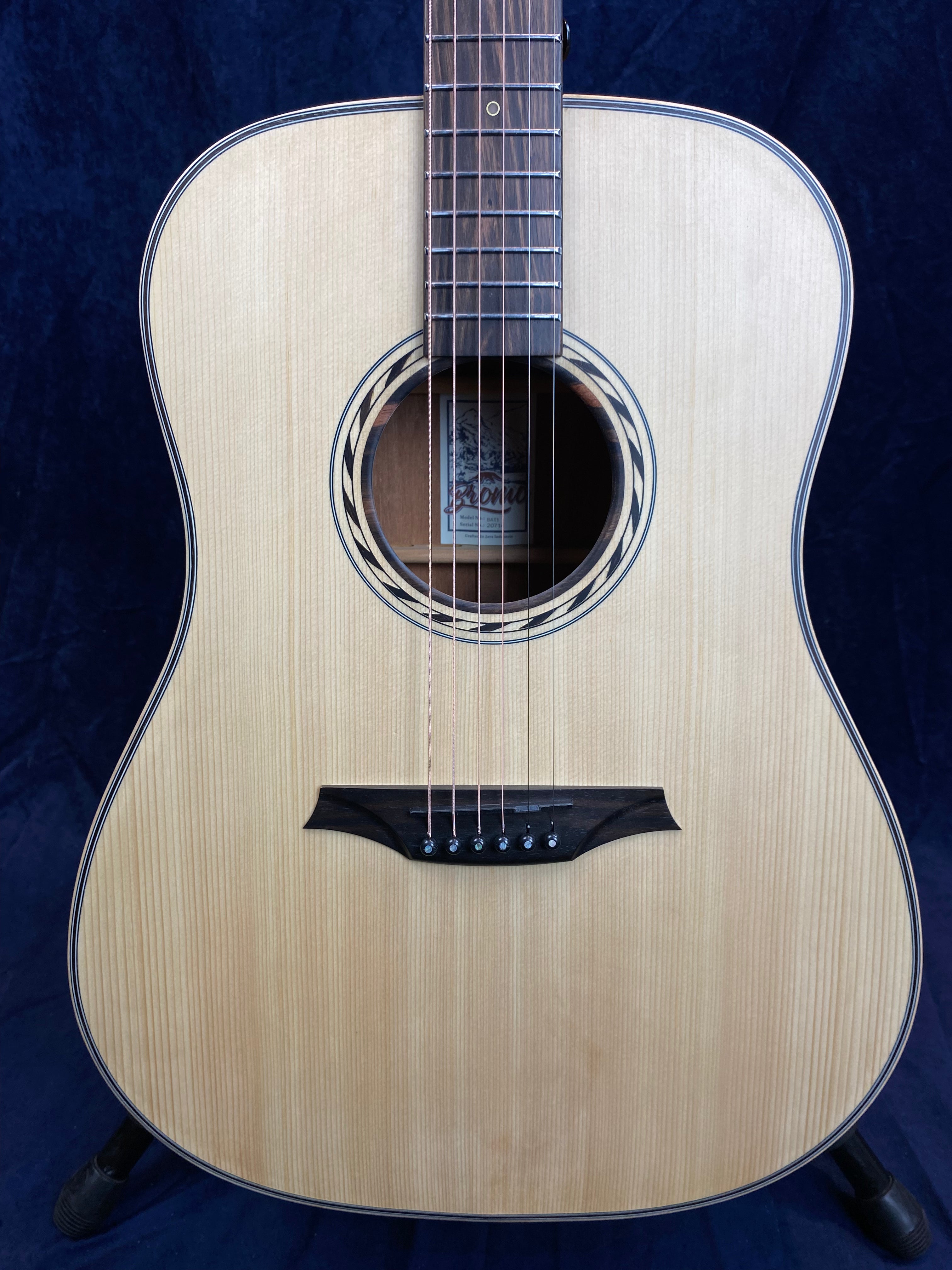 Light wood acoustic guitar with six strings, a round sound hole bordered by a patterned ring, and a dark bridge with six black pins.