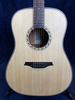 Light wood acoustic guitar with six strings, a round sound hole bordered by a patterned ring, and a dark bridge with six black pins.