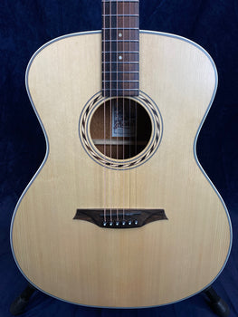 Light wood acoustic guitar with a round sound hole, simple circular rosette, dark bridge, and six strings, viewed from the front against a dark background.