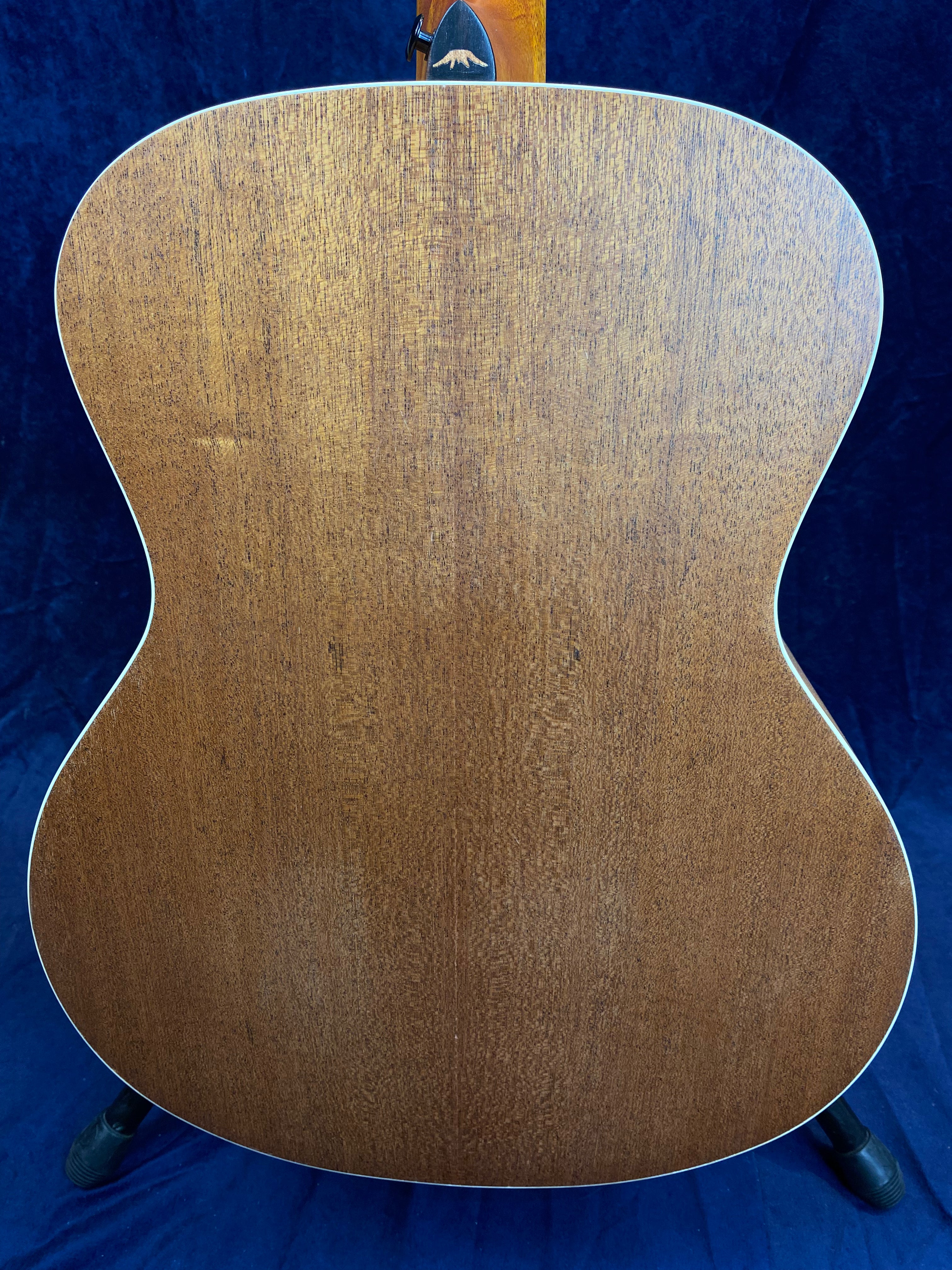 Back view of an acoustic guitar with a smooth, natural wood grain finish, outlined by thin white binding against a dark blue background.