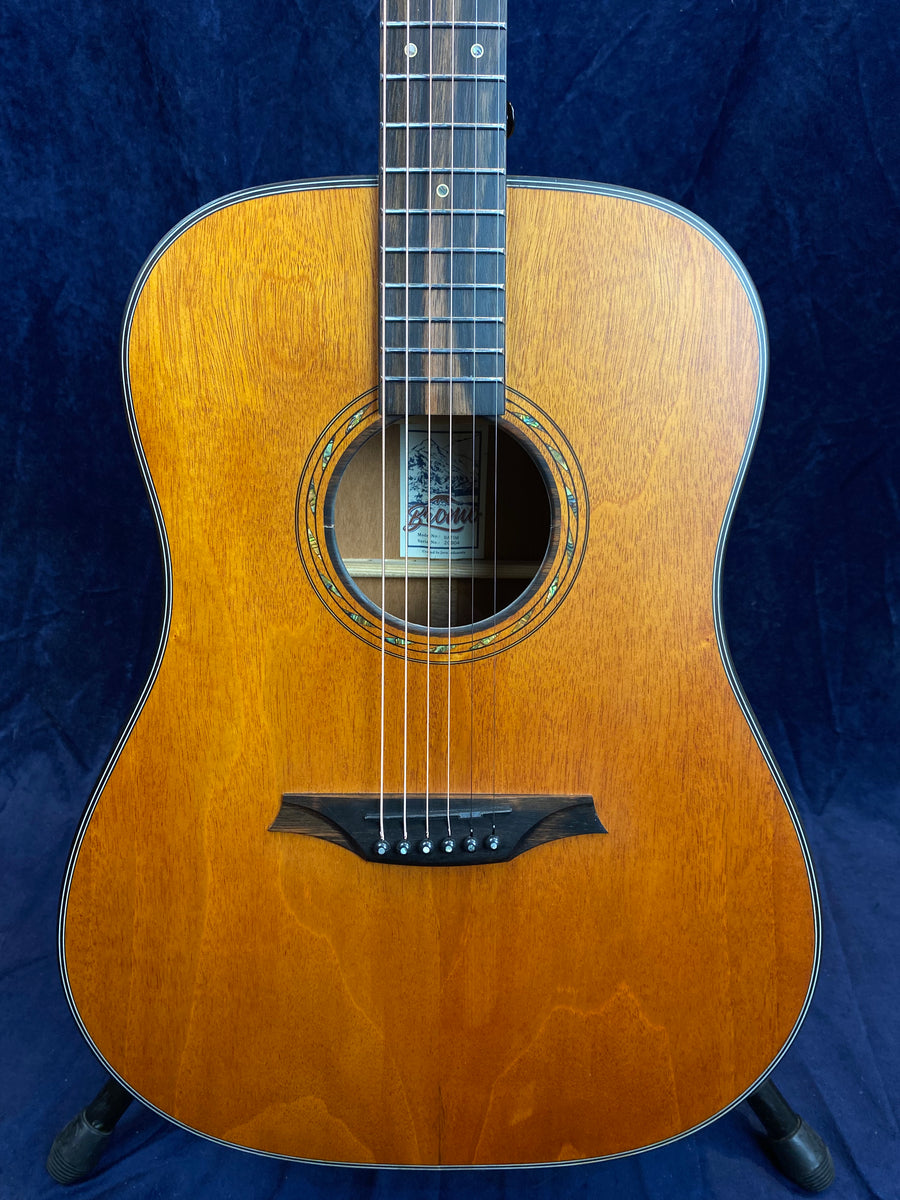 Brown acoustic guitar with a natural wood finish, six strings, decorative sound hole ring, black bridge, and a label inside the sound hole.