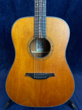 Brown acoustic guitar with a natural wood finish, six strings, decorative sound hole ring, black bridge, and a label inside the sound hole.