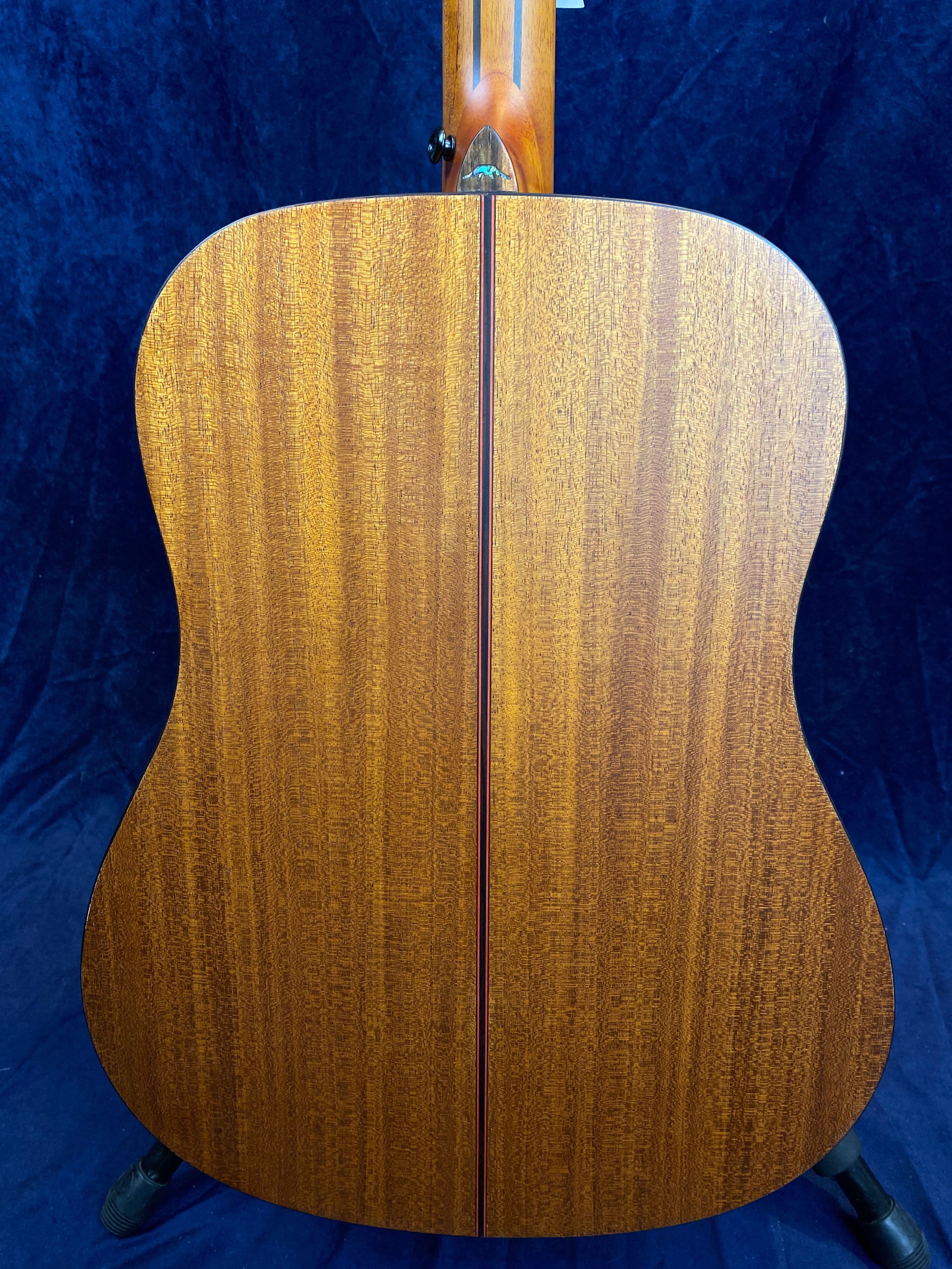 Back view of an acoustic guitar showing smooth, rich brown wood grain with a thin, darker center seam and rounded body edges.