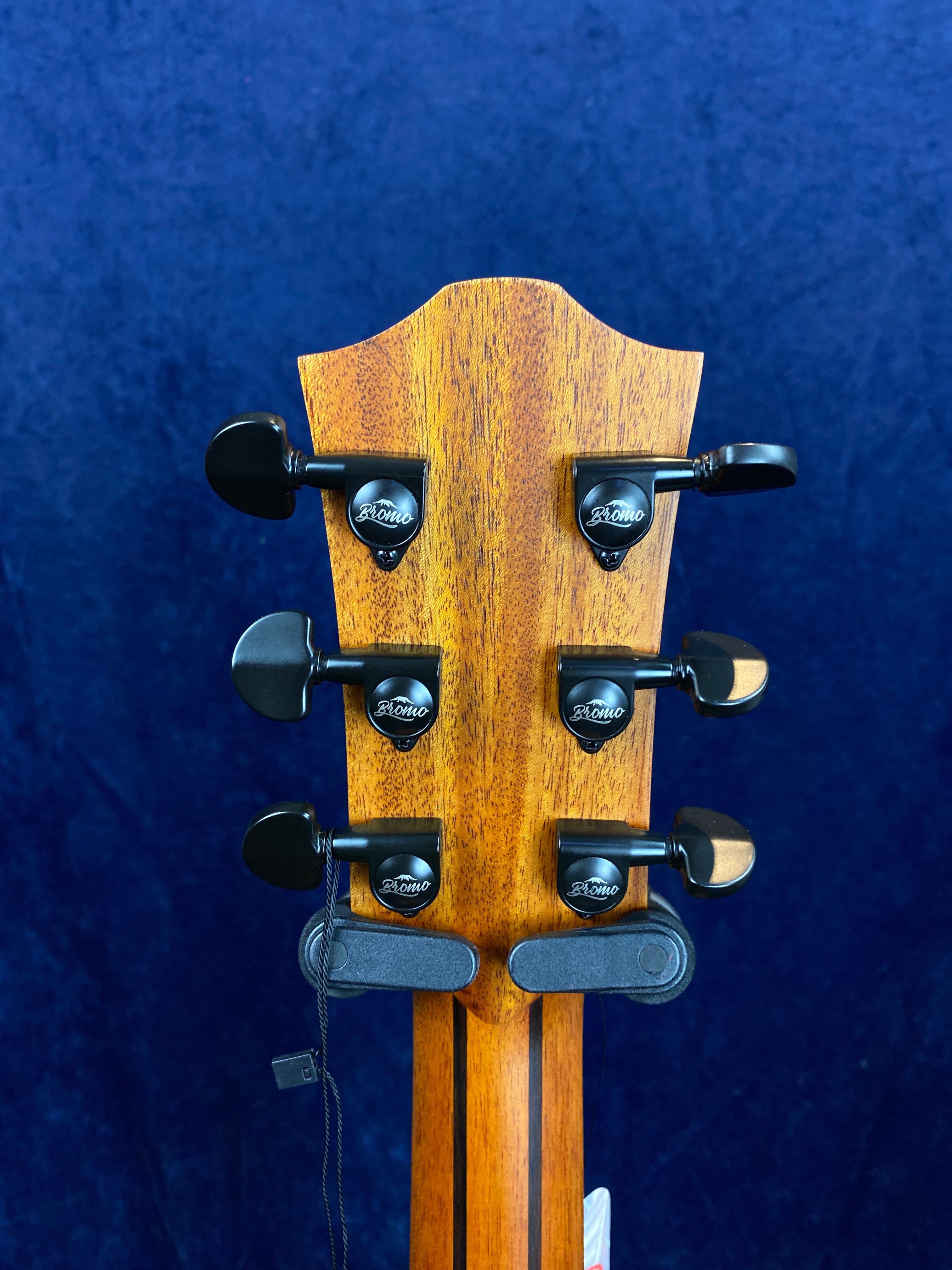 Rear view of an acoustic guitar headstock showing six black tuning pegs with "Bromo" branding against a dark blue background.