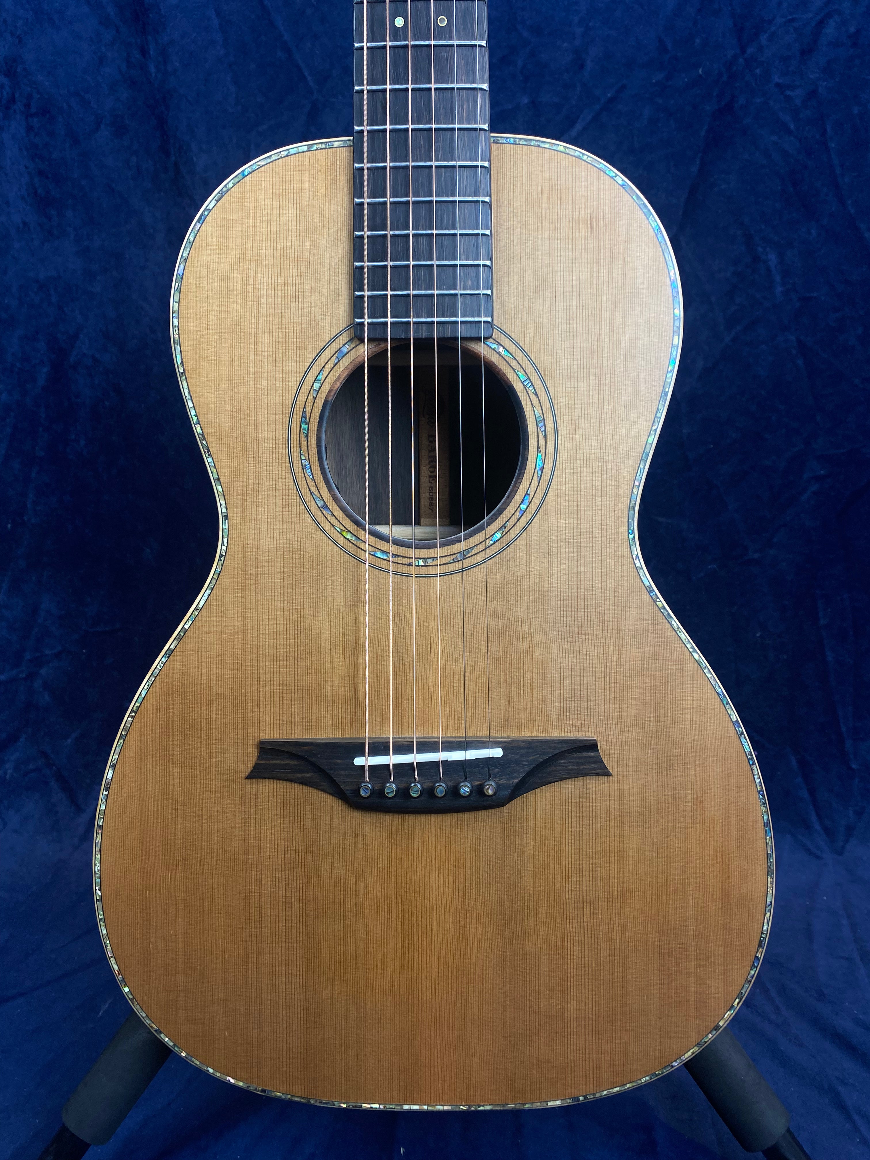 Small-bodied acoustic guitar with a natural wood finish, abalone trim around the body and soundhole, six strings, and a dark wood bridge.