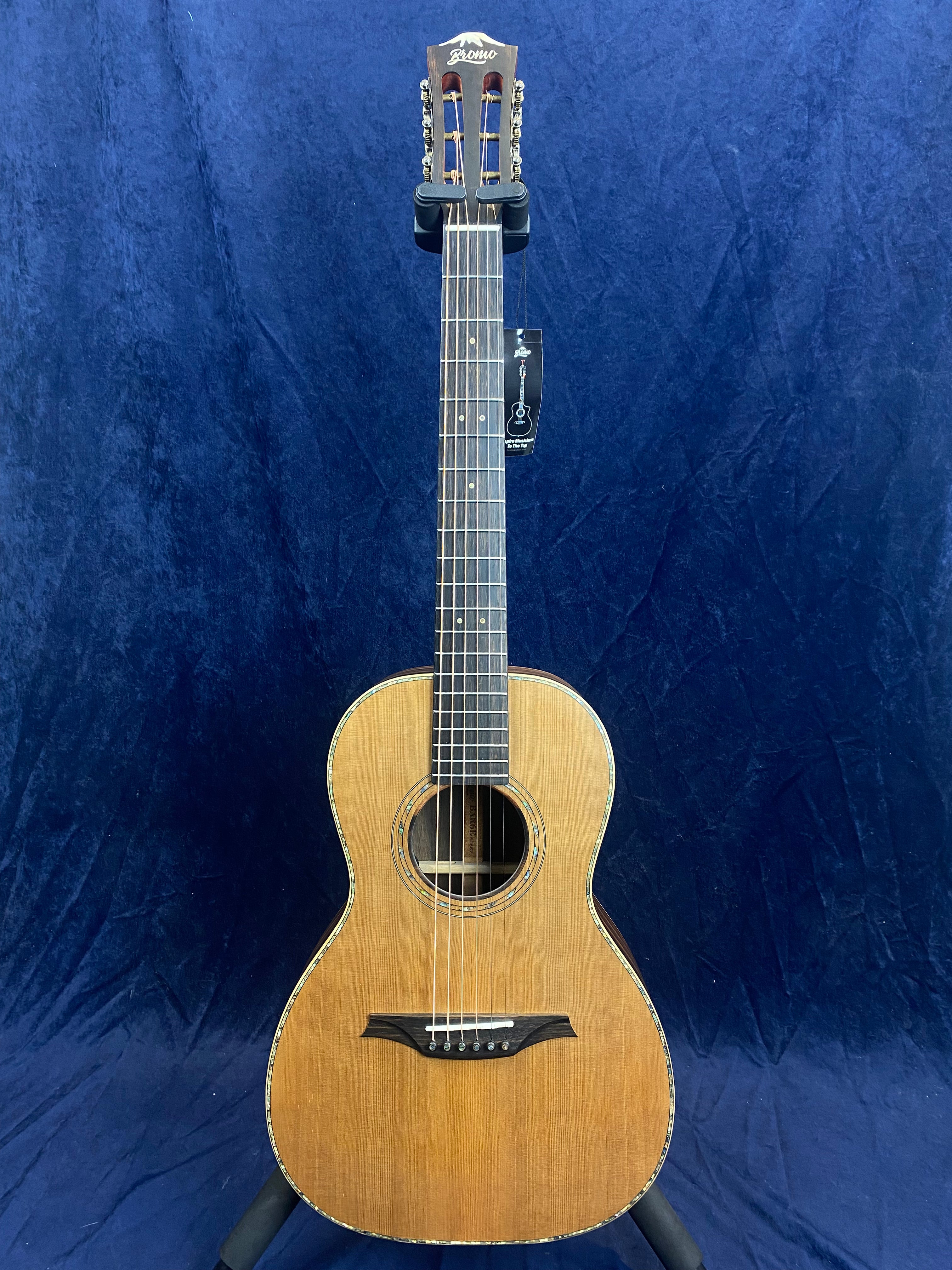 Small-bodied acoustic guitar with a natural wood finish, slotted headstock, dark fretboard, and simple decorative rosette on a blue background.
