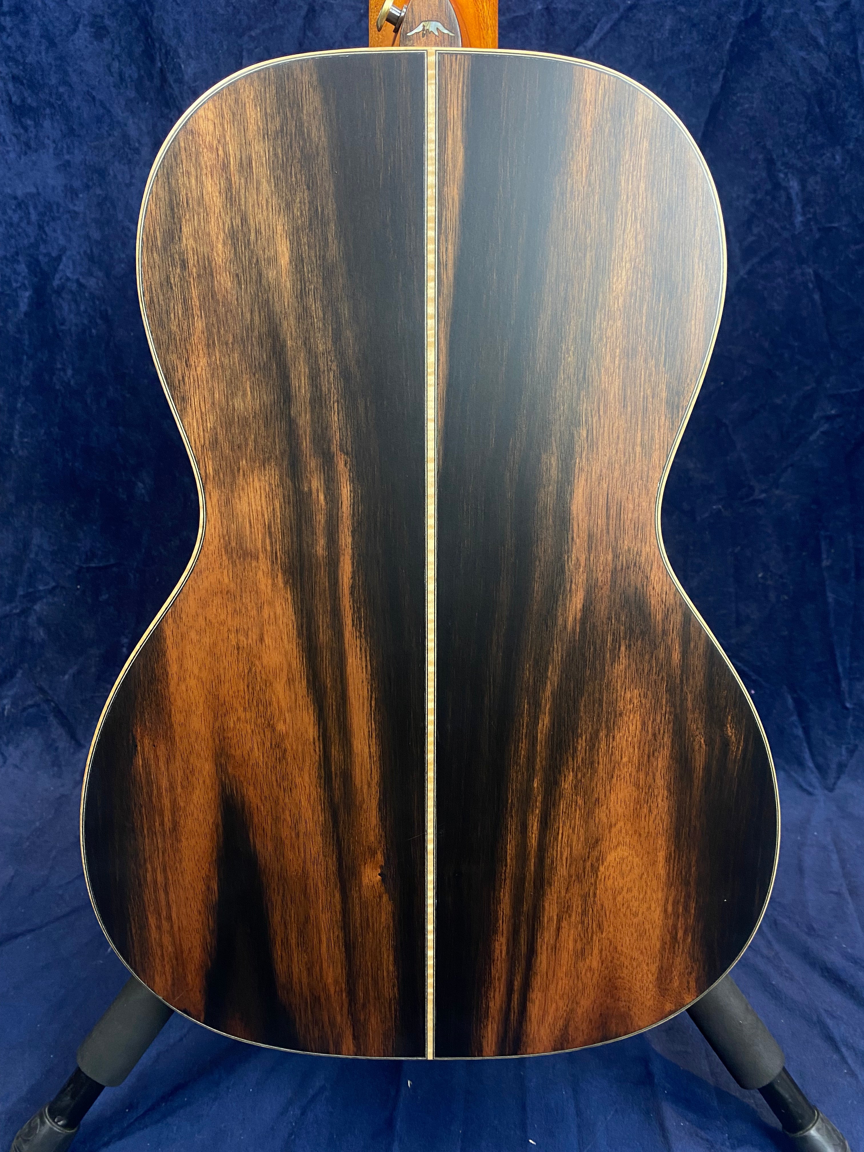 Back of an acoustic guitar showing dark wood with lighter brown streaks and a thin vertical inlay stripe down the center.