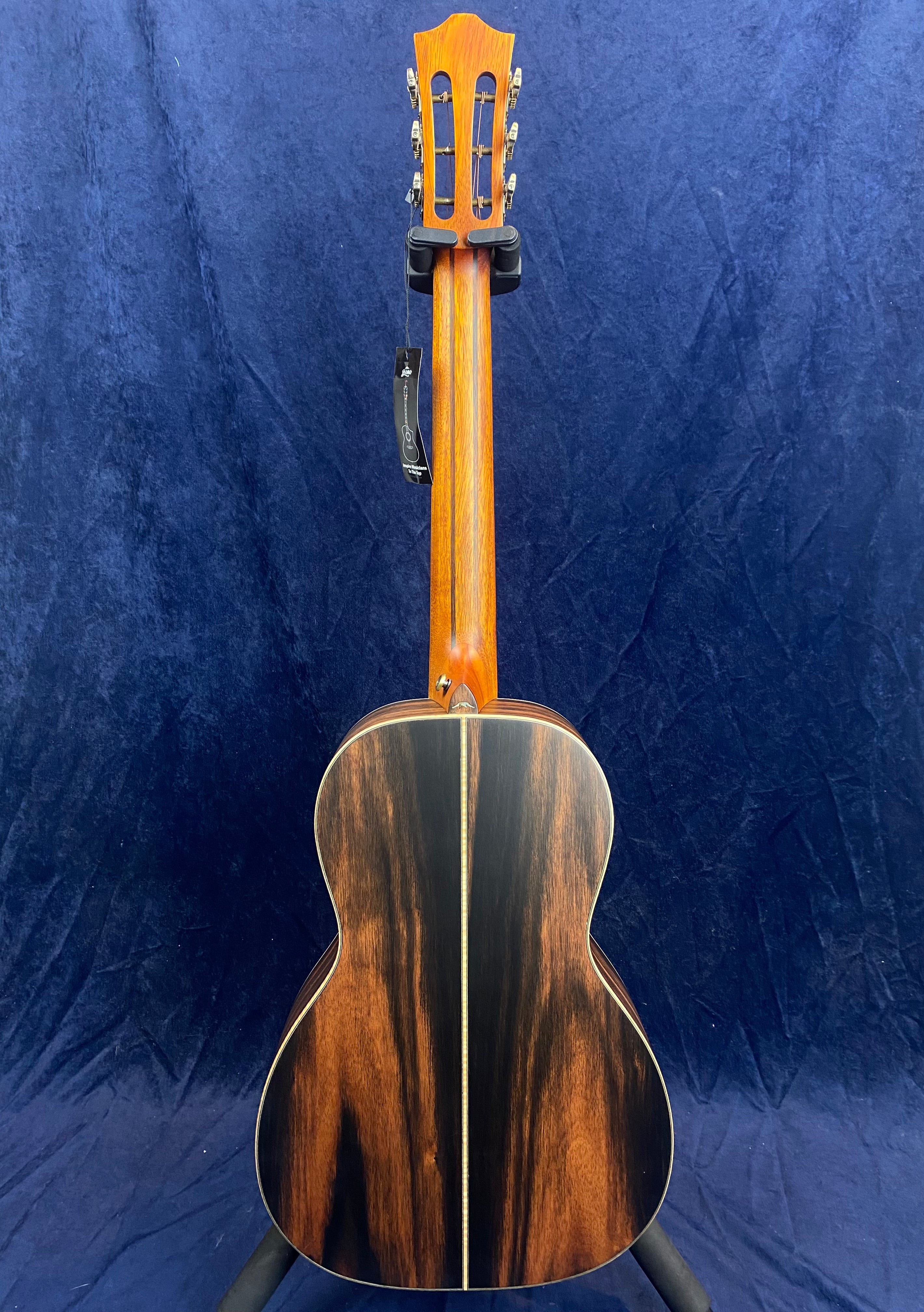The back of an acoustic guitar with a glossy, dark wood finish and a light-colored center stripe, shown upright against a blue background.