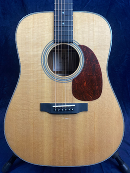 Acoustic guitar with a light wood body, black bridge, six strings, dark tortoiseshell pickguard, and concentric circle soundhole design.