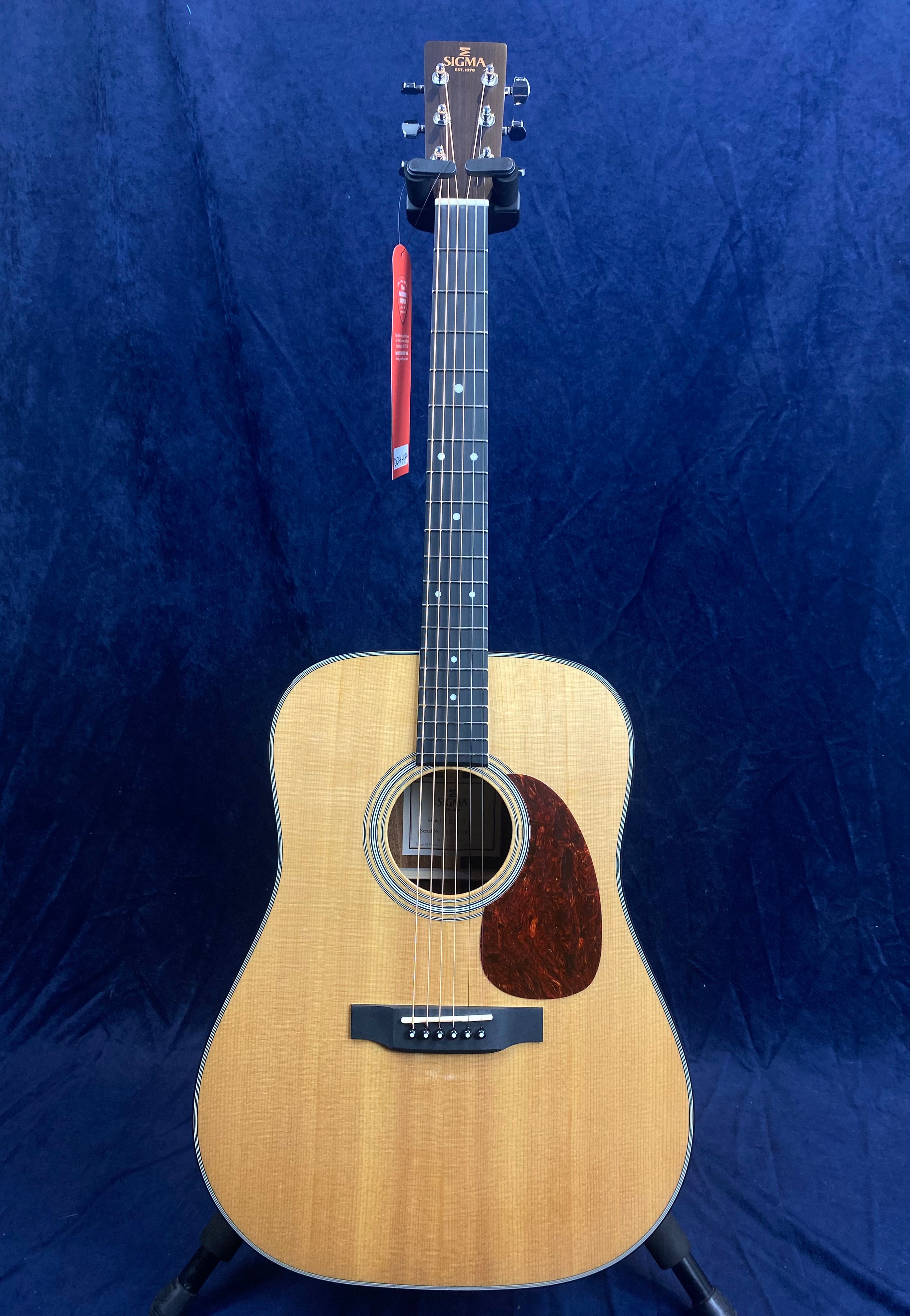 Sigma Acoustic Guitar with a natural wood finish, dark pickguard, six strings, and chrome tuning pegs against a dark blue background.