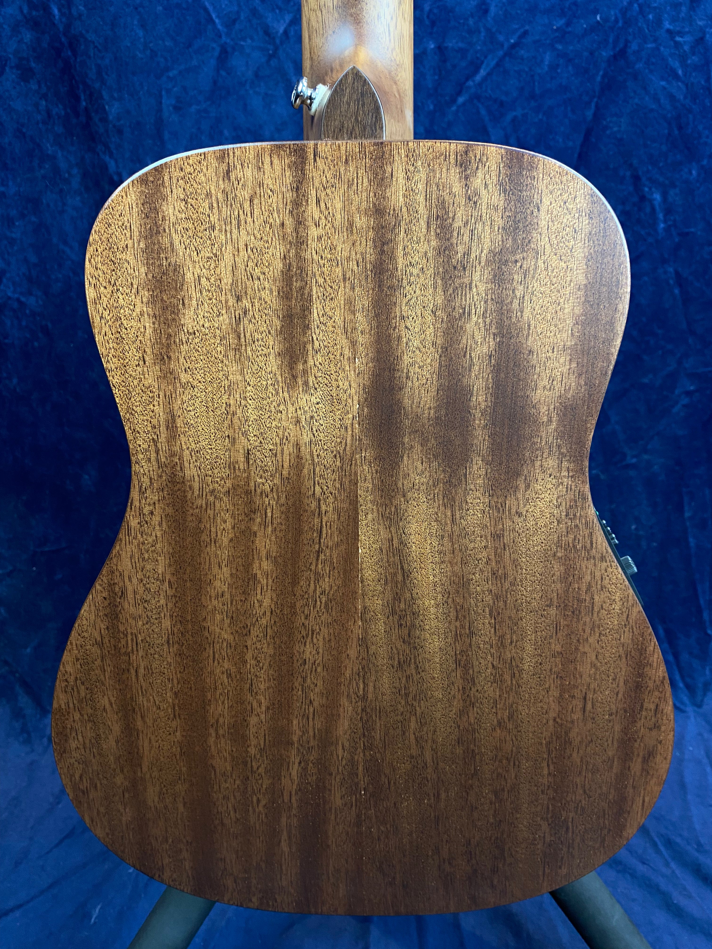Back view of an electric guitar with a natural wood finish, showing the grain pattern on a smoothly contoured, slightly curved body.