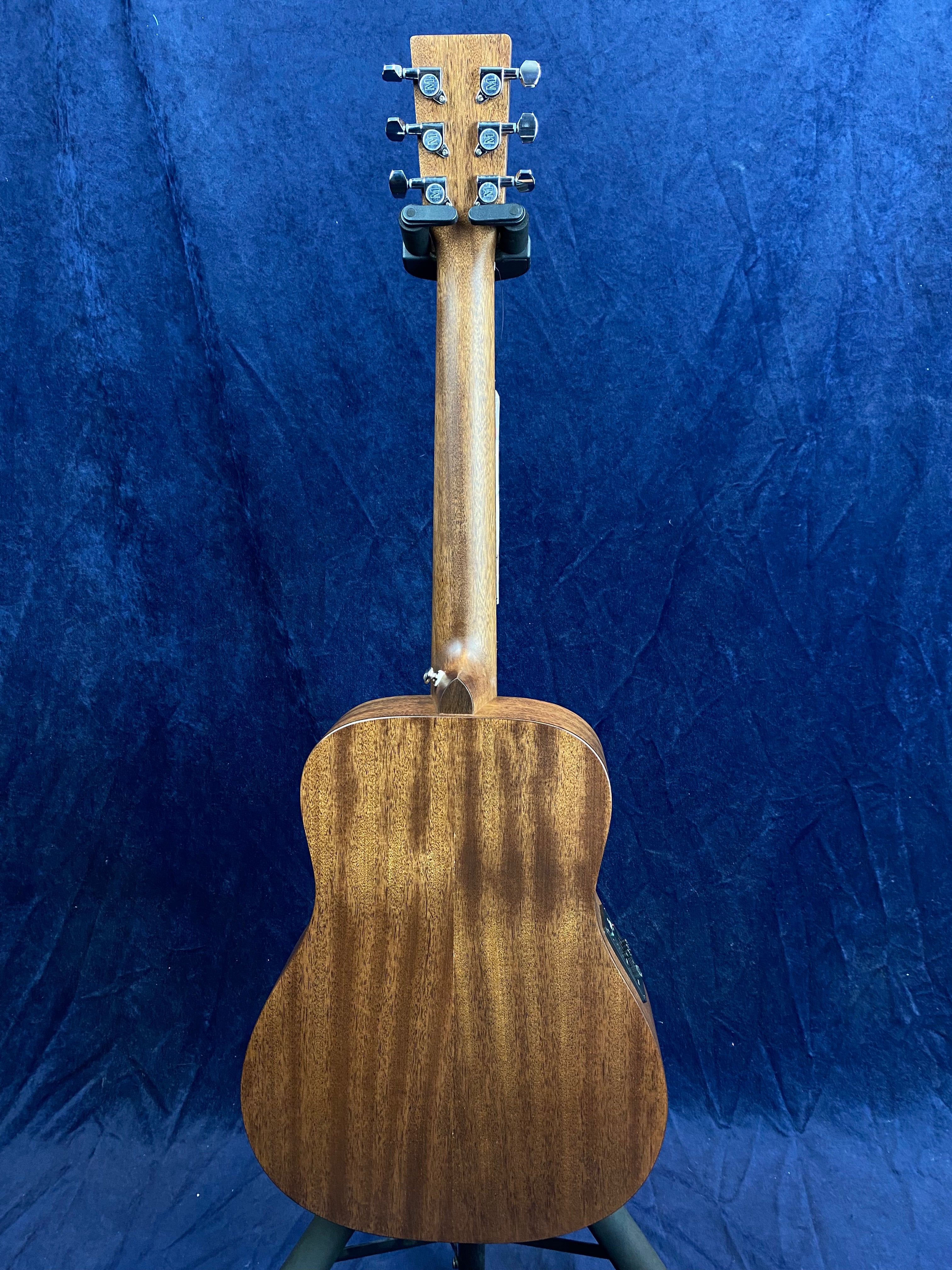 A wooden electric guitar is shown from the back, displaying natural wood grain, six tuning pegs, and a cutaway body shape against a blue background.