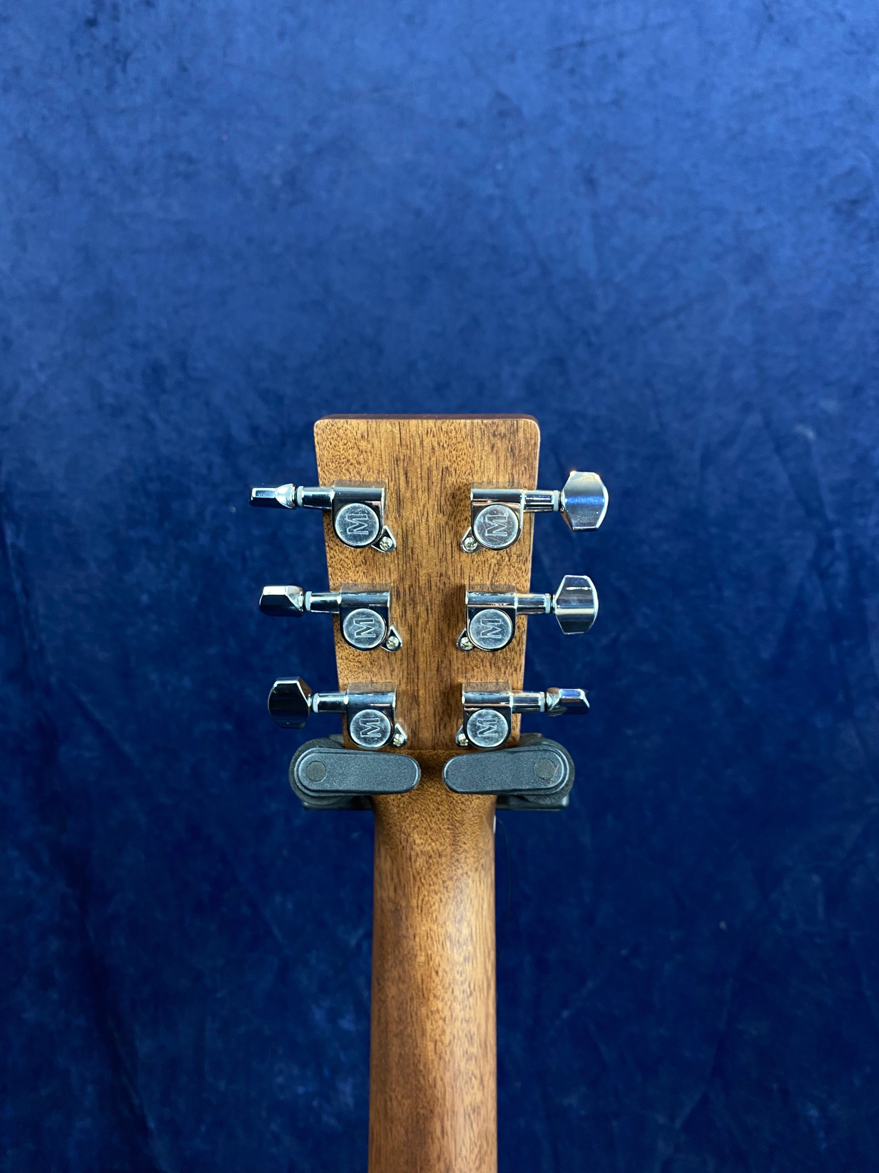 Six chrome tuning pegs on a wooden electric guitar headstock; viewed from the back against a plain dark blue background.