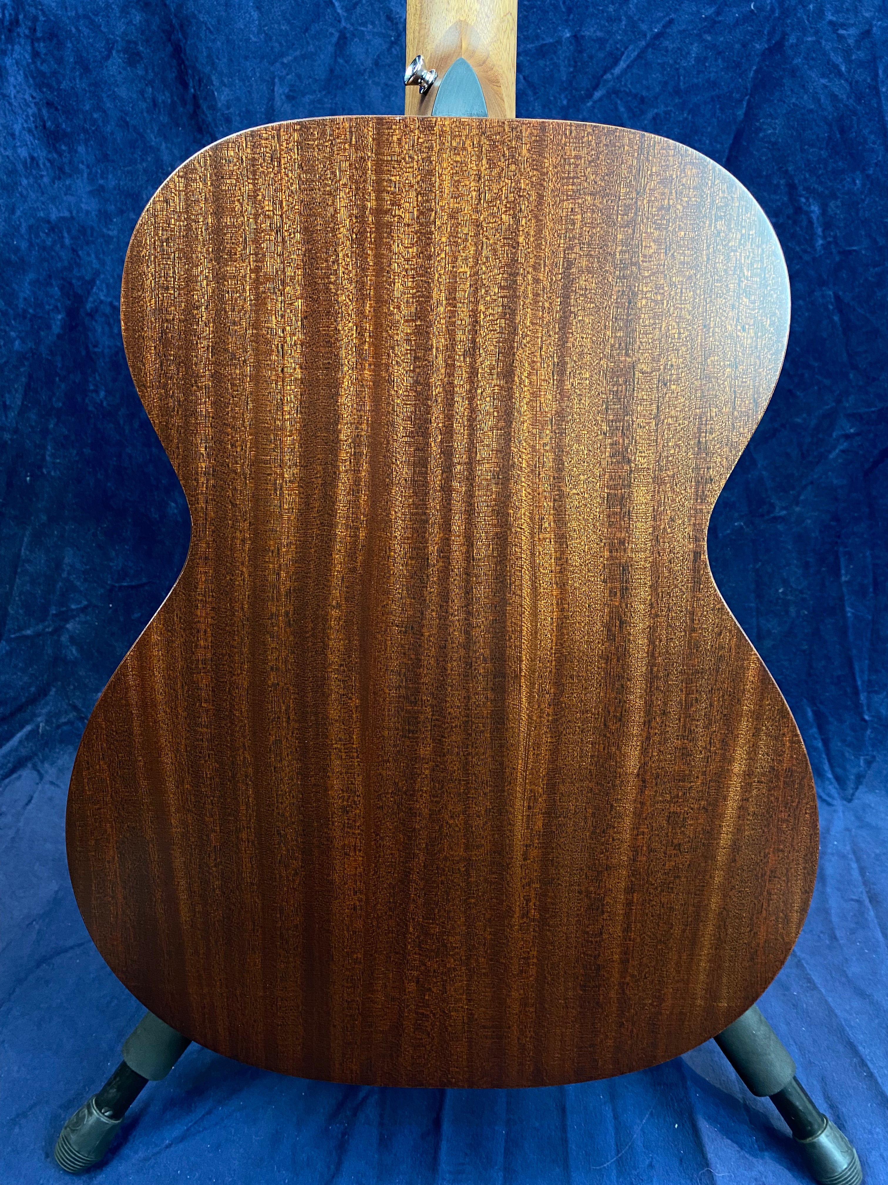 The back of an acoustic guitar made of dark, reddish-brown wood with a straight, vertical grain pattern, displayed against a blue background.
